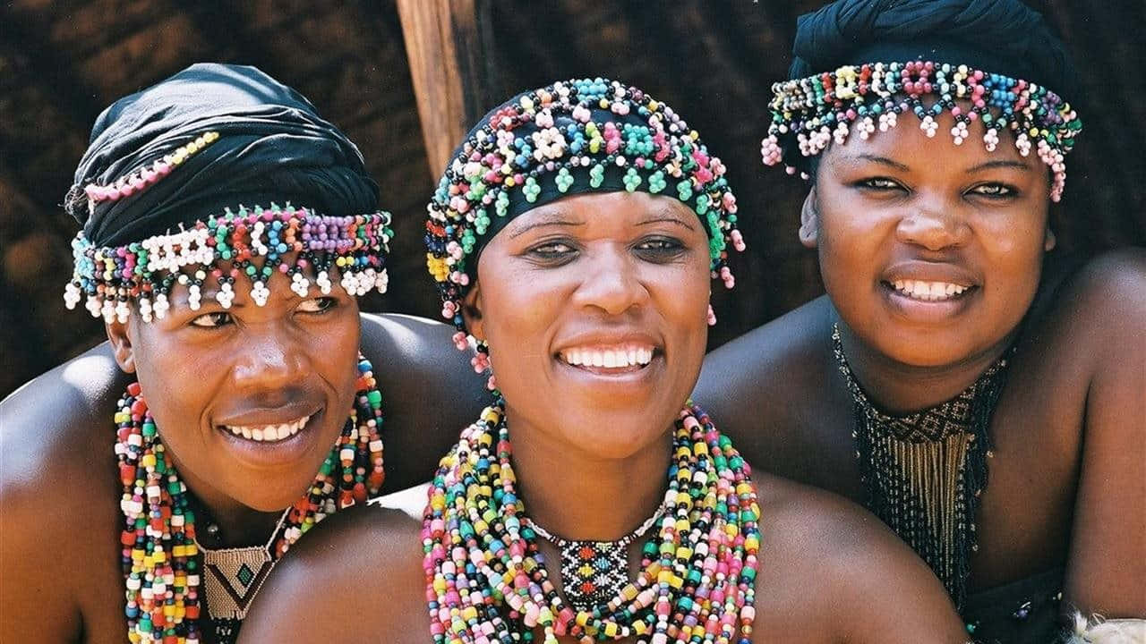 African Culture 桌布 壁紙 — 三位微笑的女性戴著鮮豔的珠飾頭帶和項鍊，在戶外緊密地擺姿勢。
