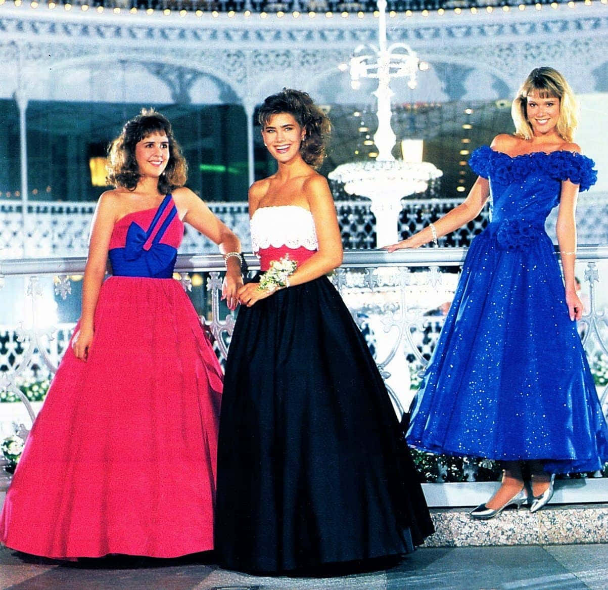 80s Aesthetic 桌布 壁紙 — 三位微笑的女性穿著鮮豔的1980年代舞會禮服，在夜晚於裝飾性噴泉旁優雅地擺姿勢。