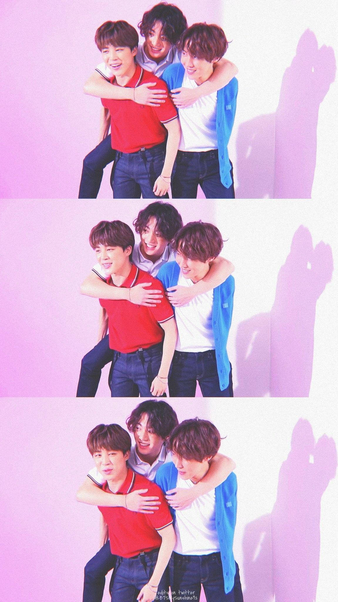 jhope 桌布 壁紙 — 三位微笑的年輕男子穿著休閒服裝，在柔和的粉紅色工作室牆前熱情擁抱，他們俏皮的影子投射在身後。