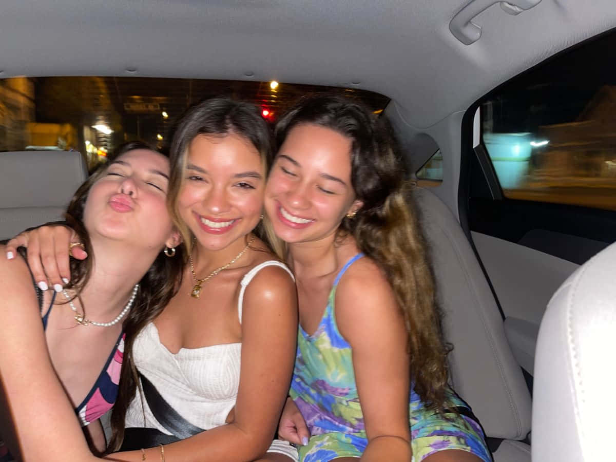 Friends 桌布 壁紙 — 三位微笑的朋友在夜晚的車內頑皮地擺姿勢，模糊的城市燈光從窗外掠過。