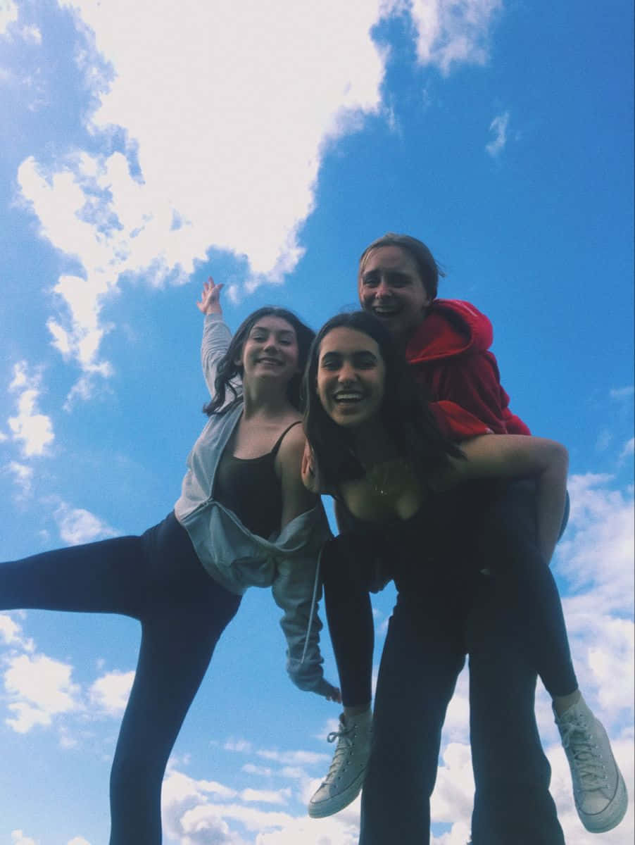 Friends 桌布 壁紙 — 三位微笑的朋友在明亮的藍天和蓬鬆的白雲下頑皮地擺姿勢。