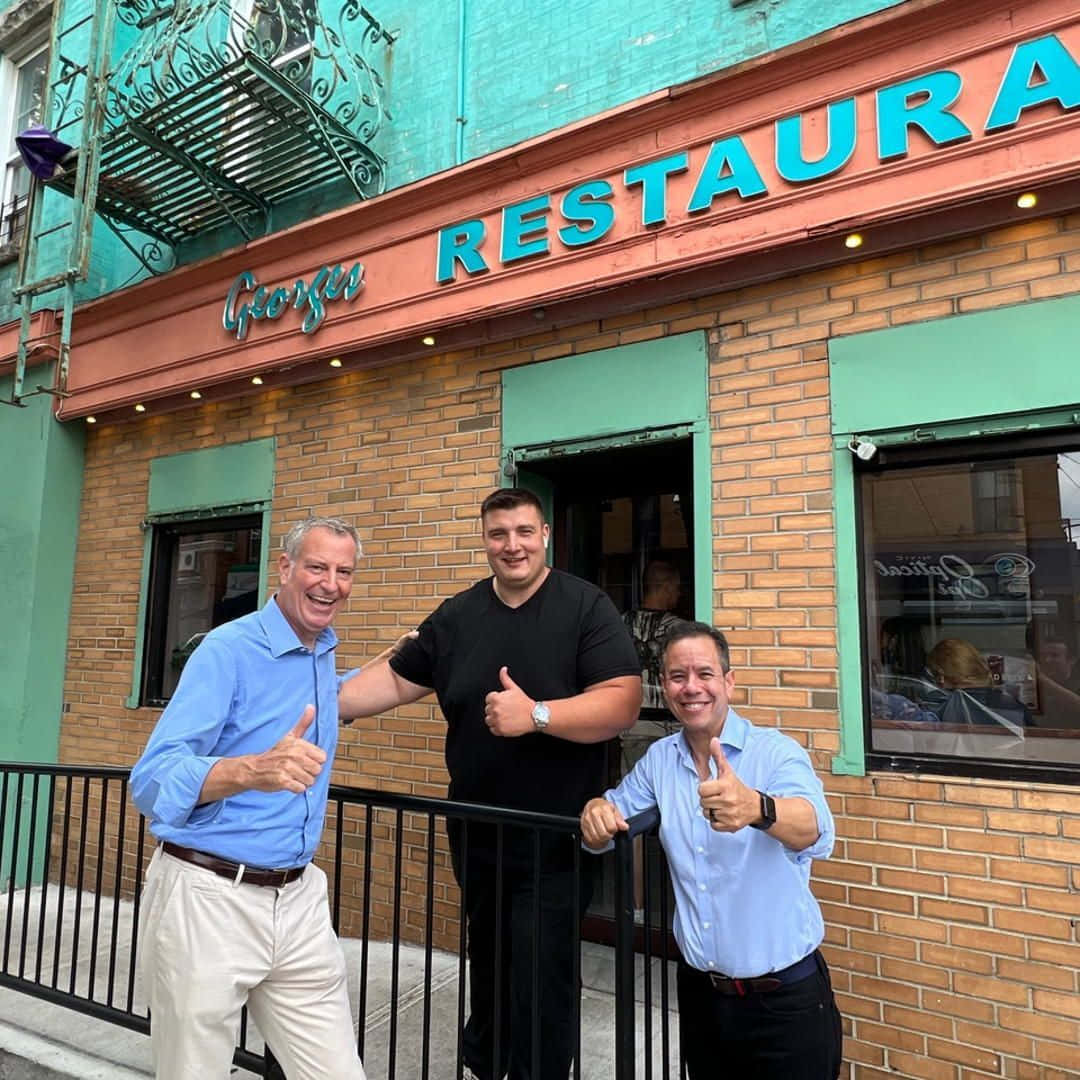Restaurant 桌布 壁紙 — 三位微笑的男人在一間有青綠色飾邊和復古招牌的磚砌餐廳外面豎起大拇指。