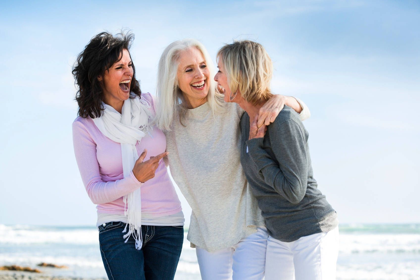 3 Best Friends 桌布 壁紙 — 三位快樂的女性在陽光明媚的海灘上一起大笑，身後是海洋的波浪。