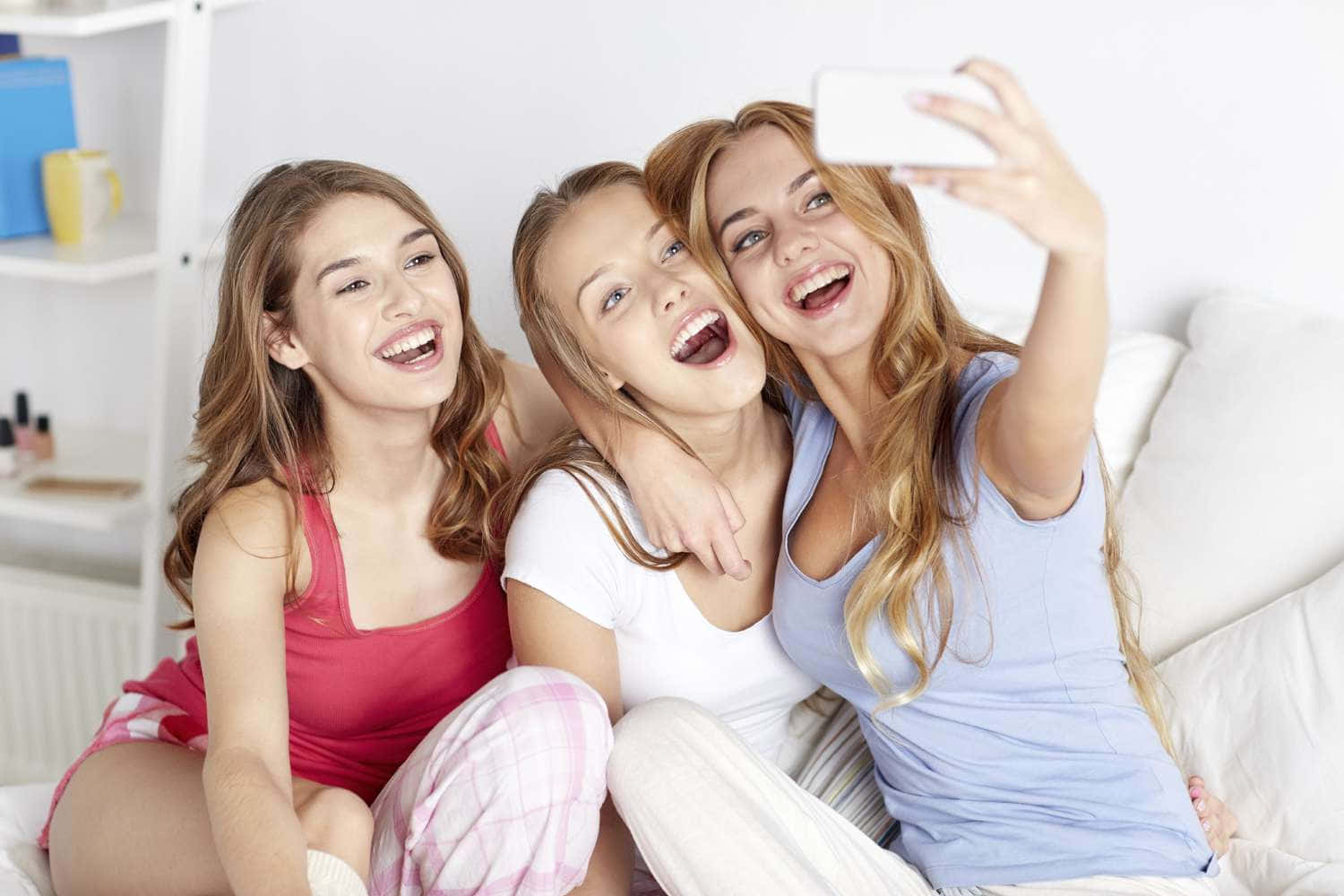 girls 桌布 壁紙 — 三位快樂的年輕女性在明亮的室內白色沙發上笑著自拍。