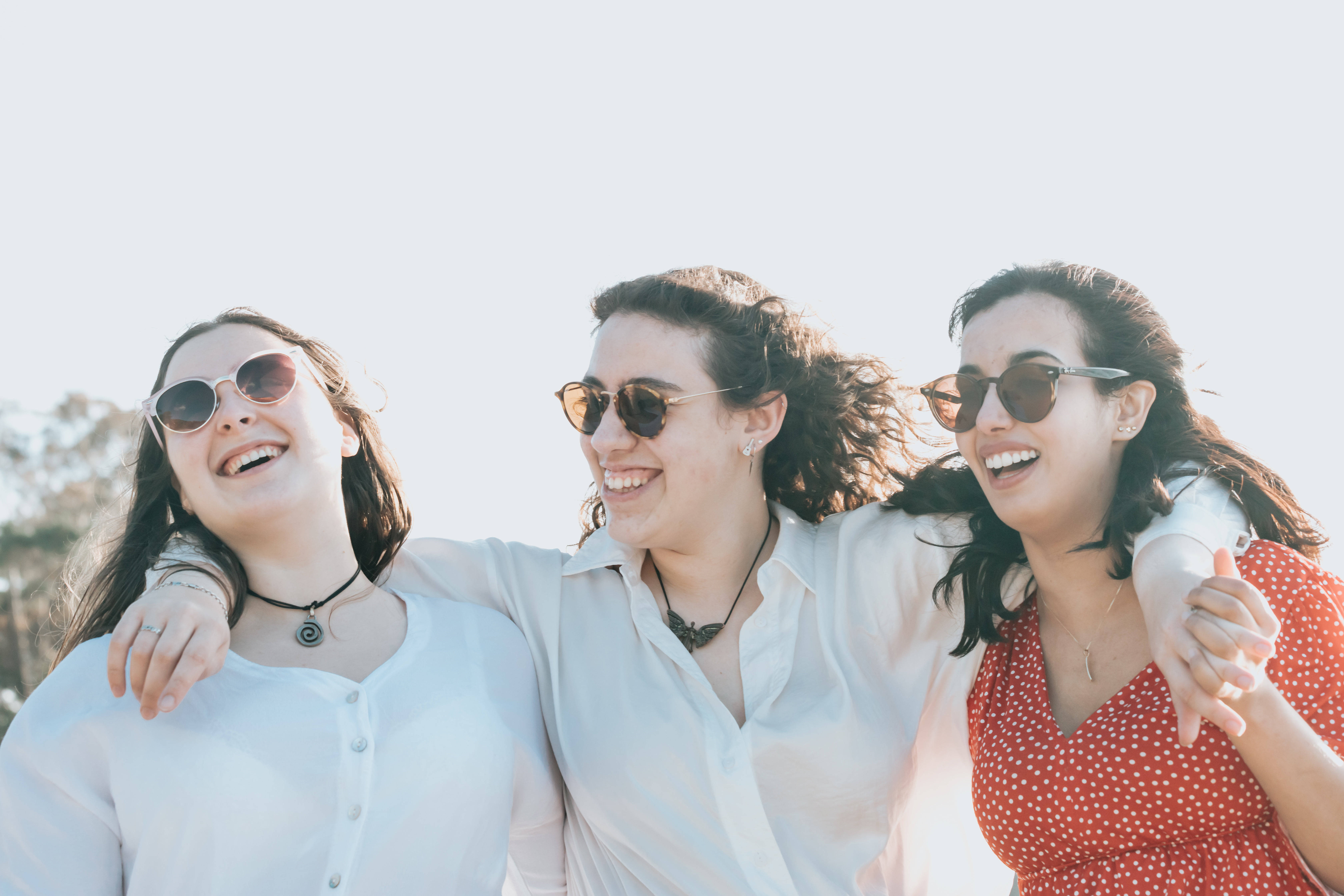 Friendship 桌布 壁紙 — 三位快樂的朋友在明亮的陽光下戴著太陽眼鏡和休閒夏裝，一起在戶外大笑。