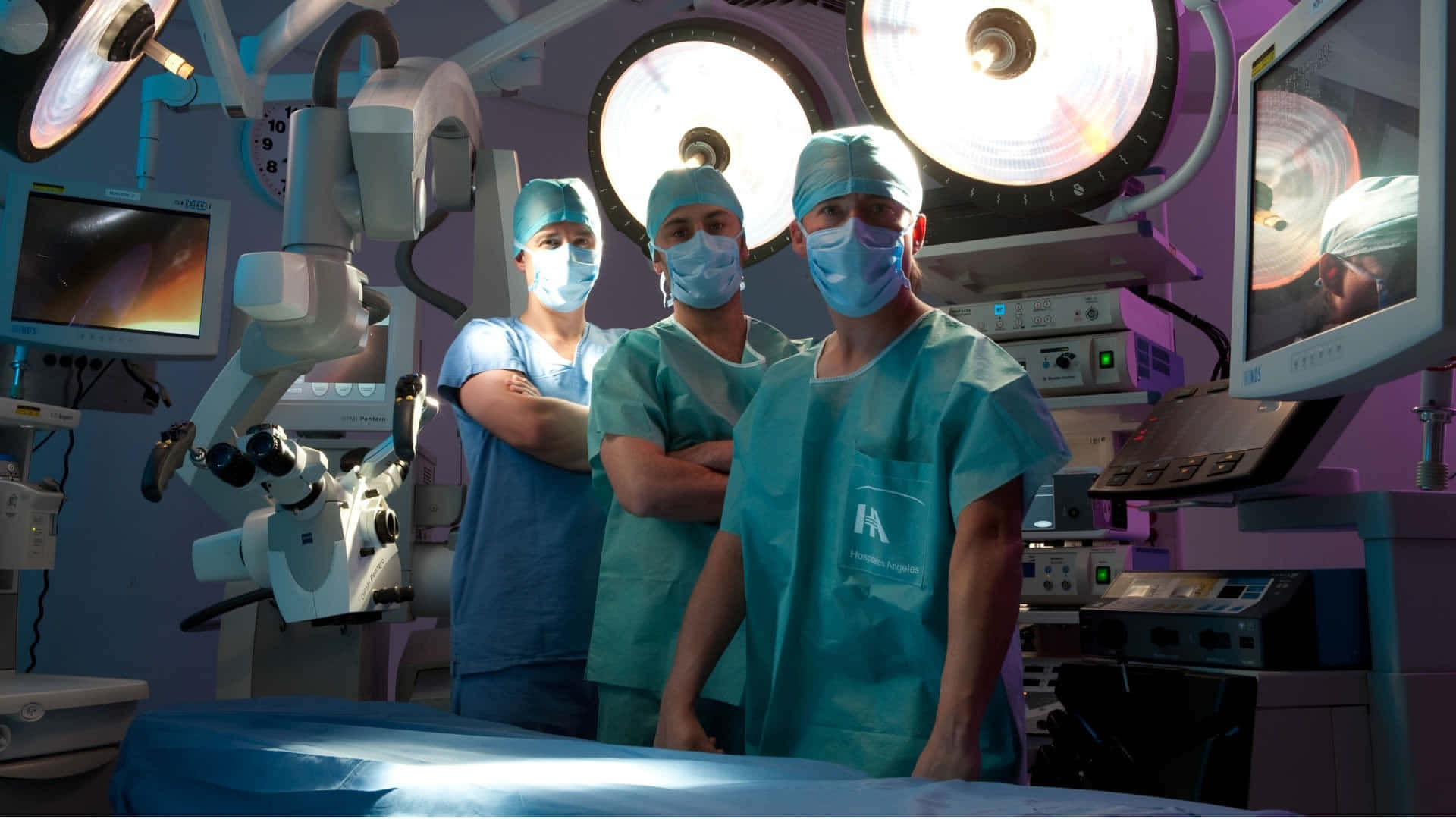 Surgery 桌布 壁紙 — 三位戴著口罩的外科醫生穿著青綠色手術服，在明亮手術燈下的高科技手術室中自信地站立。