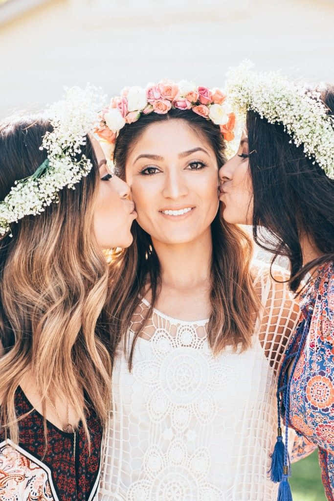 Bridesmaids 桌布 壁紙 — 三位戴著花冠的女性在戶外親吻一位微笑著、身穿白色蕾絲上衣的女性。