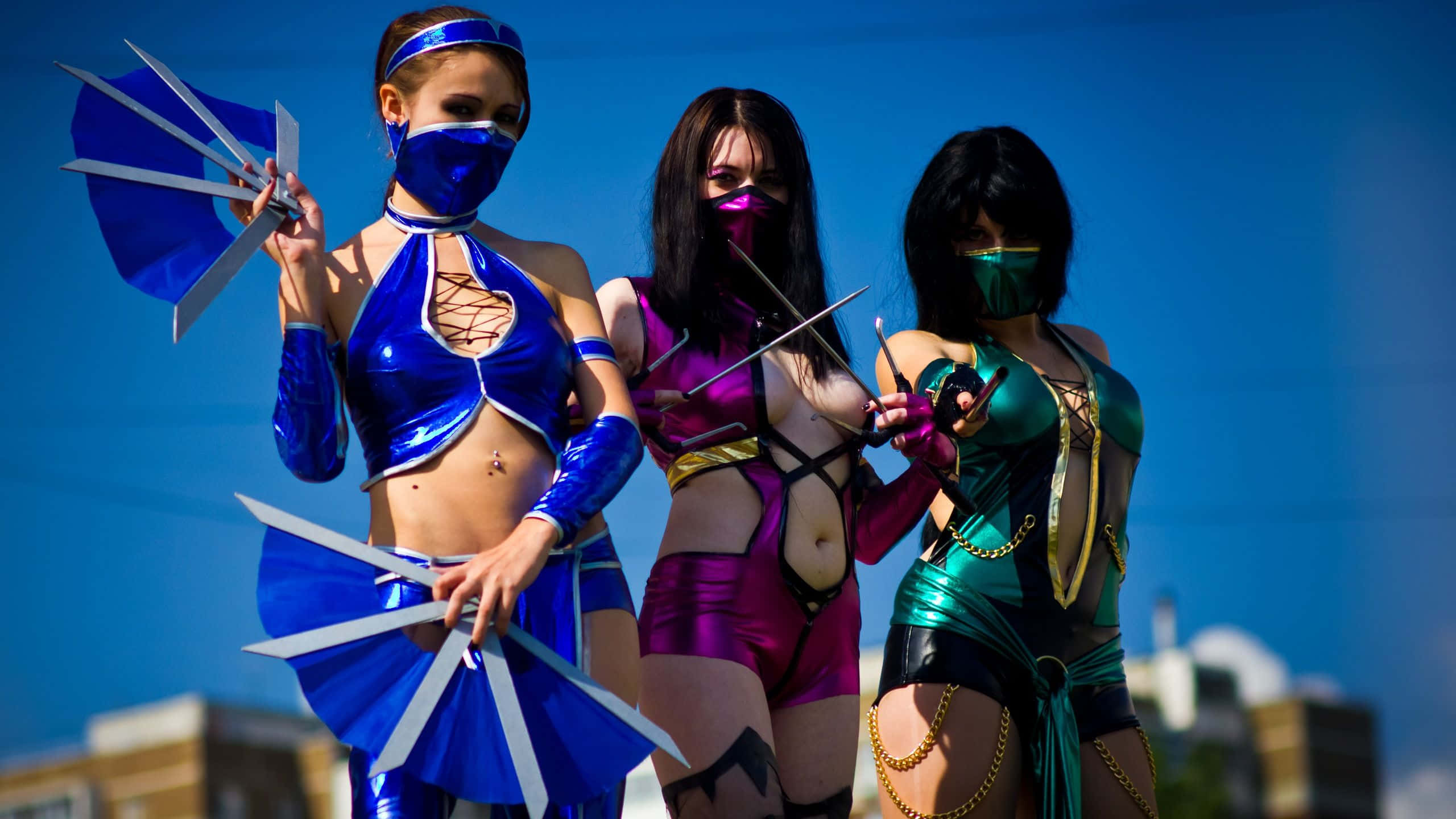 Mortal Kombat Cosplays 桌布 壁紙 — 三位戴面具的cosplayer，穿著閃亮的藍色、紫色和綠色服裝，在晴朗的藍天背景下，擺姿勢拿著風扇葉片。