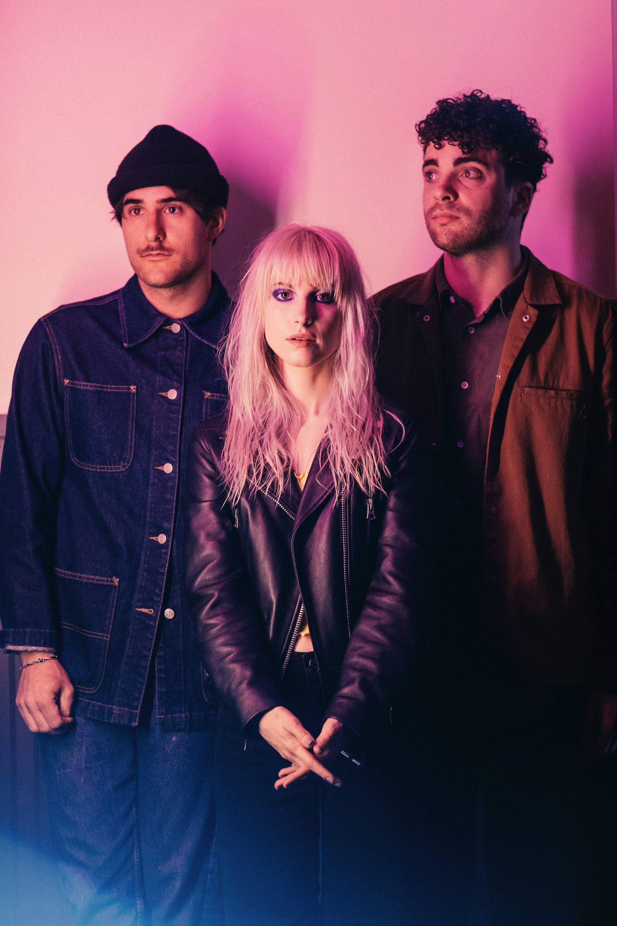 Paramore 桌布 壁紙 — 三位時尚人士在戲劇性的工作室燈光下，於充滿活力的粉紅和藍色漸變牆前擺姿勢。