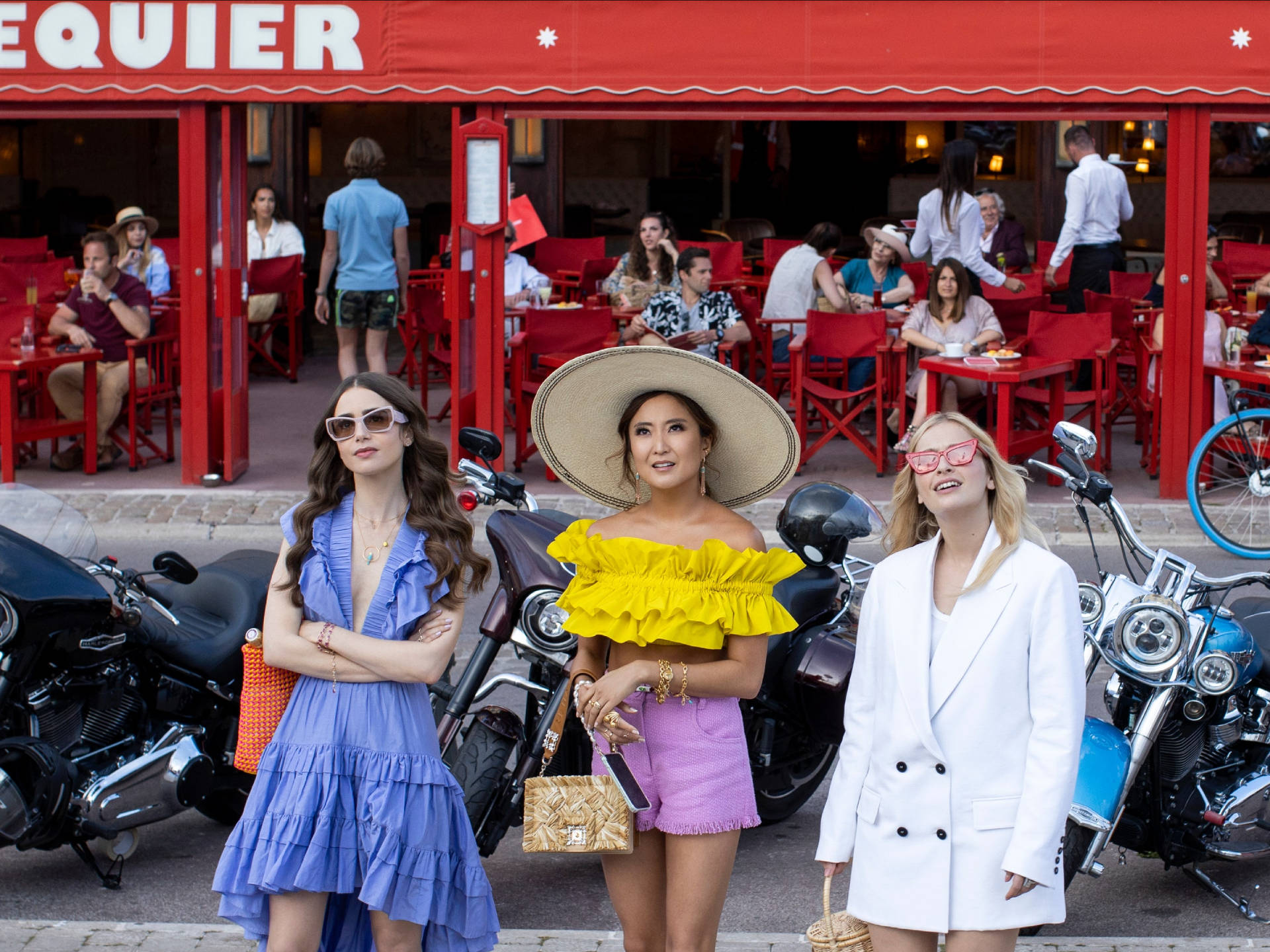 Sunglasses 桌布 壁紙 — 三位時尚女性穿著鮮豔服裝，在繁忙的戶外咖啡館的紅色遮陽篷下自信地擺姿勢，旁邊是摩托車。