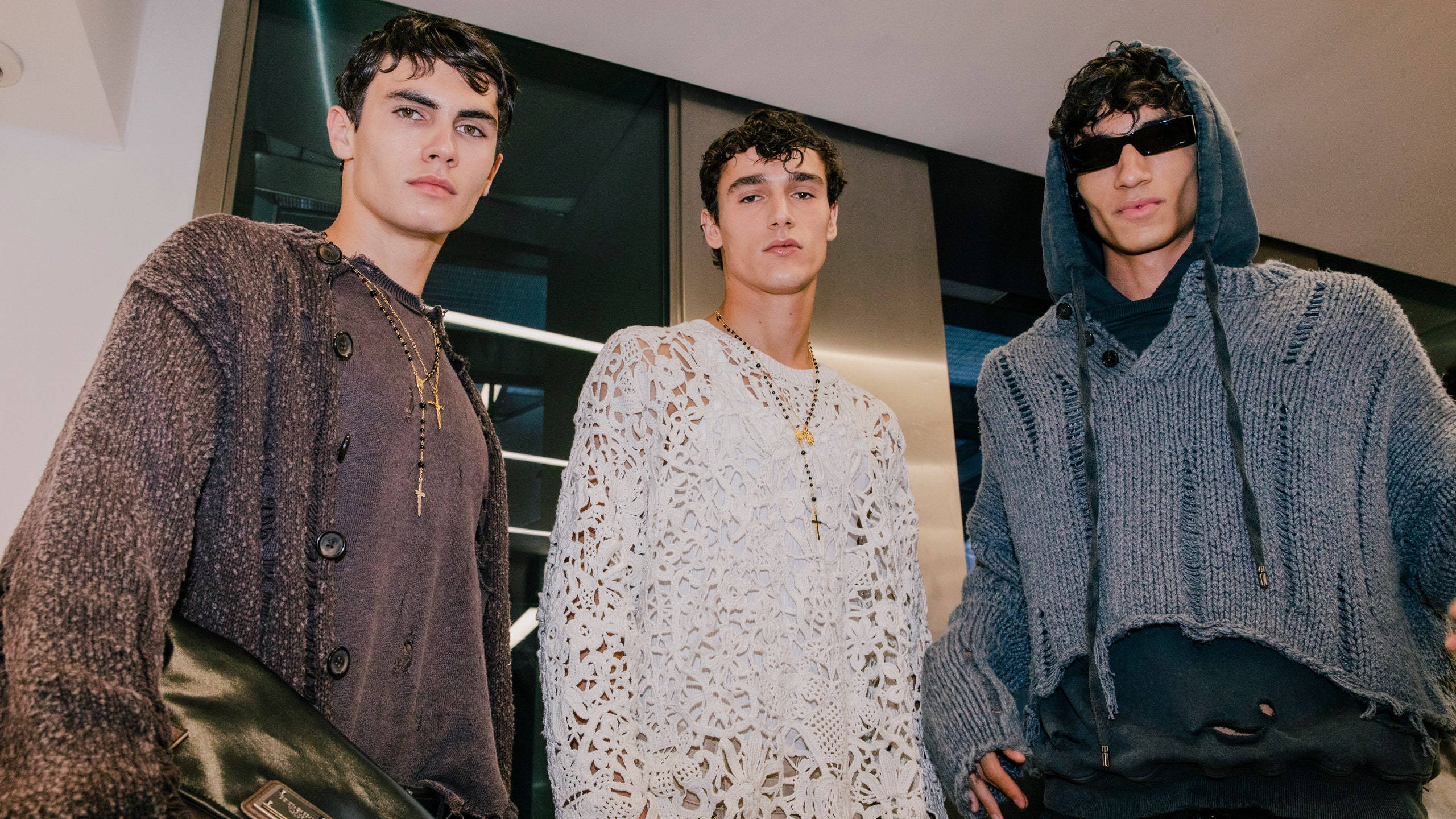 Men 桌布 壁紙 — 三位時尚年輕男士自信地穿著質感針織服裝，在現代玻璃牆室內擺姿勢。
