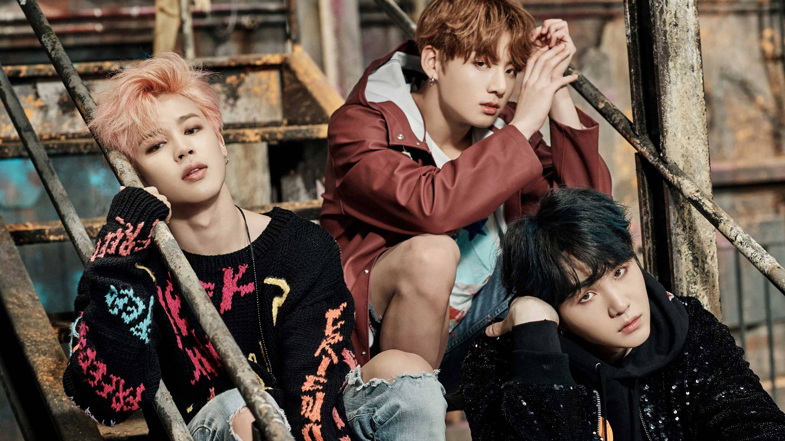 BTS 桌布 壁紙 — 三位時尚年輕男子在粗糙的城市環境中自信地站在生鏽的金屬樓梯上擺姿勢。