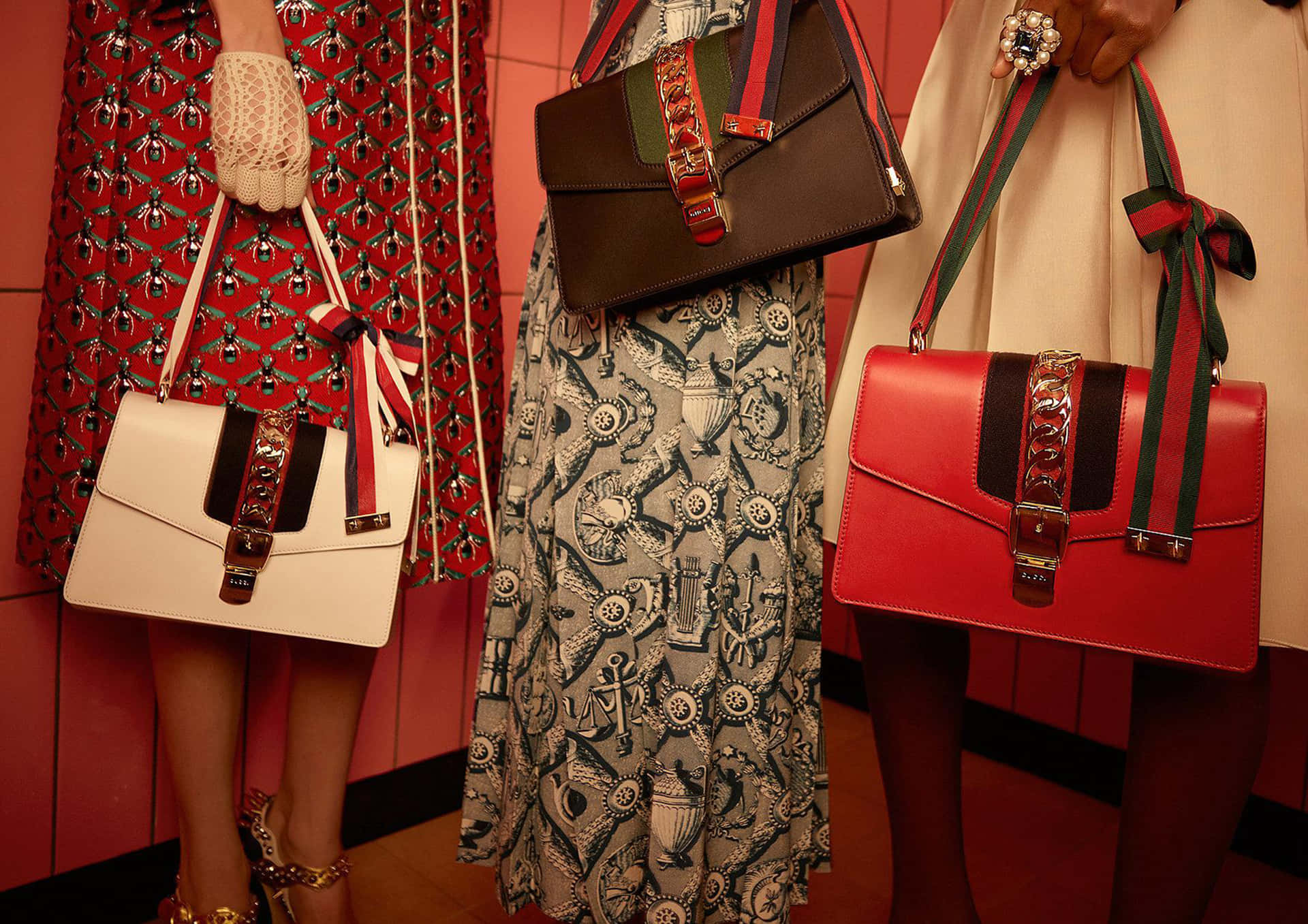 Gucci 桌布 壁紙 — 三位時尚打扮的人物在時裝秀場景中，以溫暖的紅色瓷磚牆為背景展示Gucci手袋。