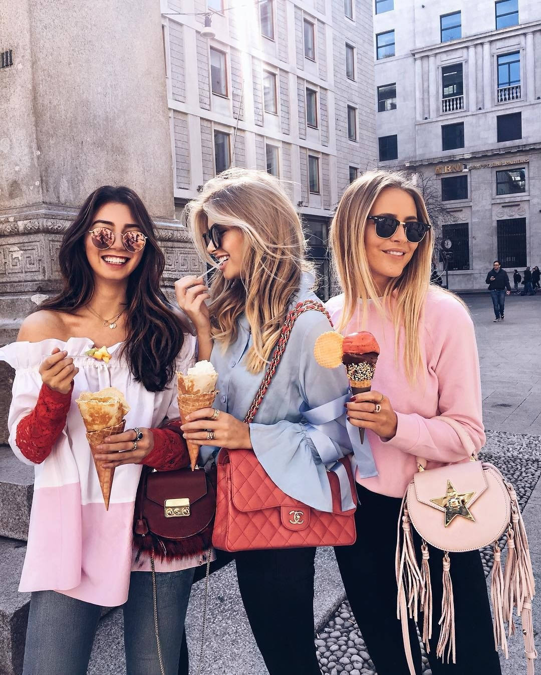3 Best Friends 桌布 壁紙 — 三位時尚朋友在陽光普照的城市廣場上，一邊享用冰淇淋甜筒，一邊大笑，背後是歷史建築。