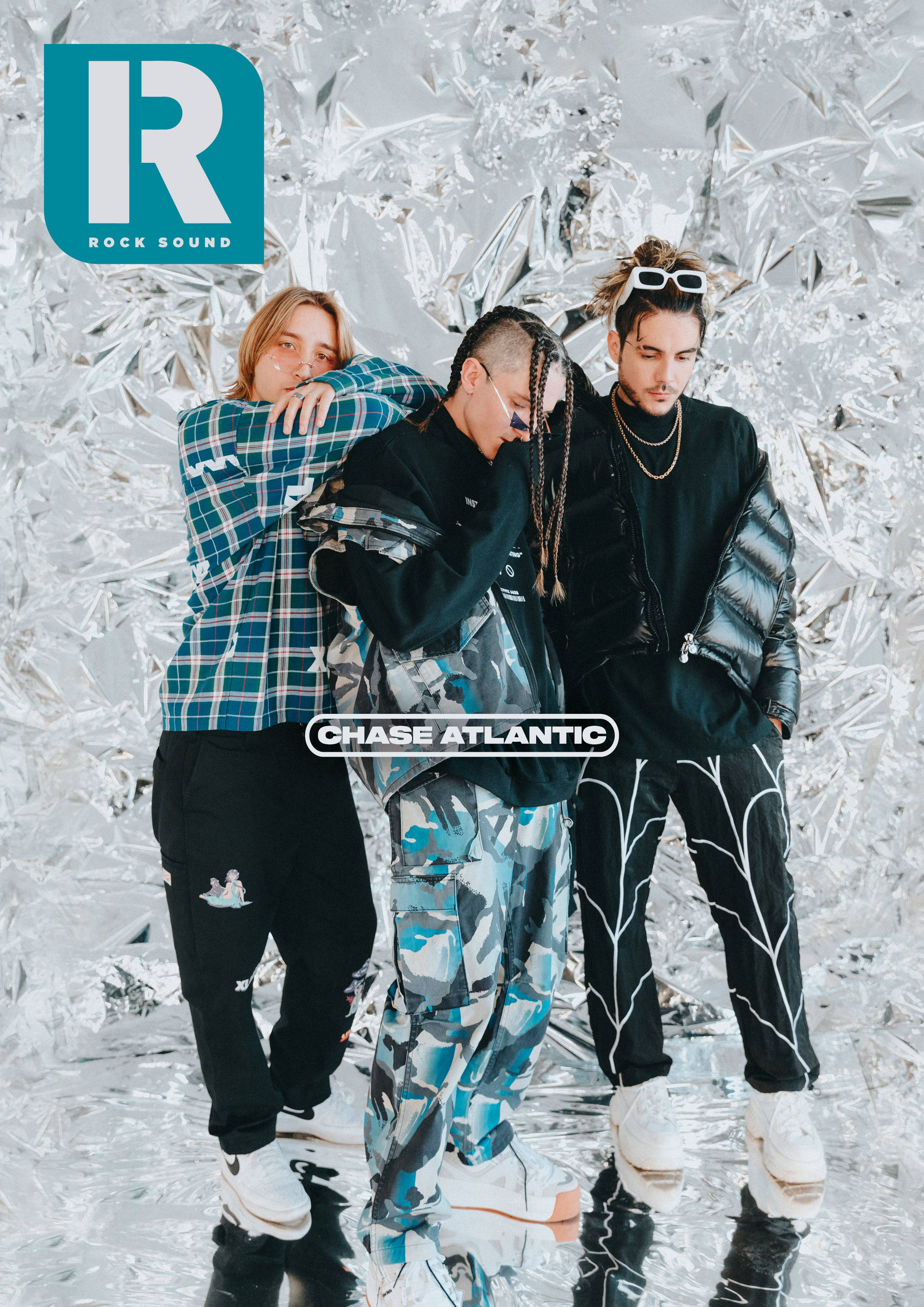 Chase Atlantic 桌布 壁紙 — 三位時尚音樂人在閃爍銀色箔紙背景和反光地板上自信地擺姿勢。