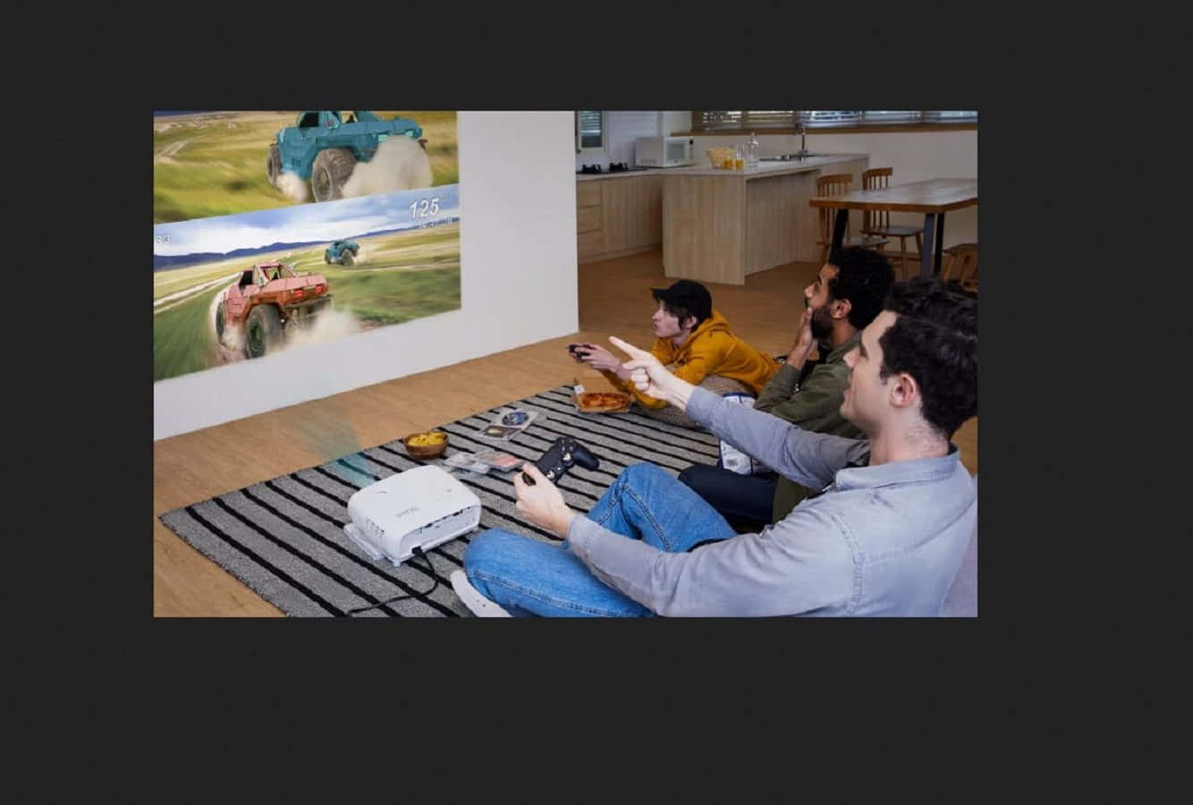 Home Entertainment 桌布 壁紙 — 三位朋友坐在地毯上，玩著投射在現代客廳牆上的賽車遊戲。