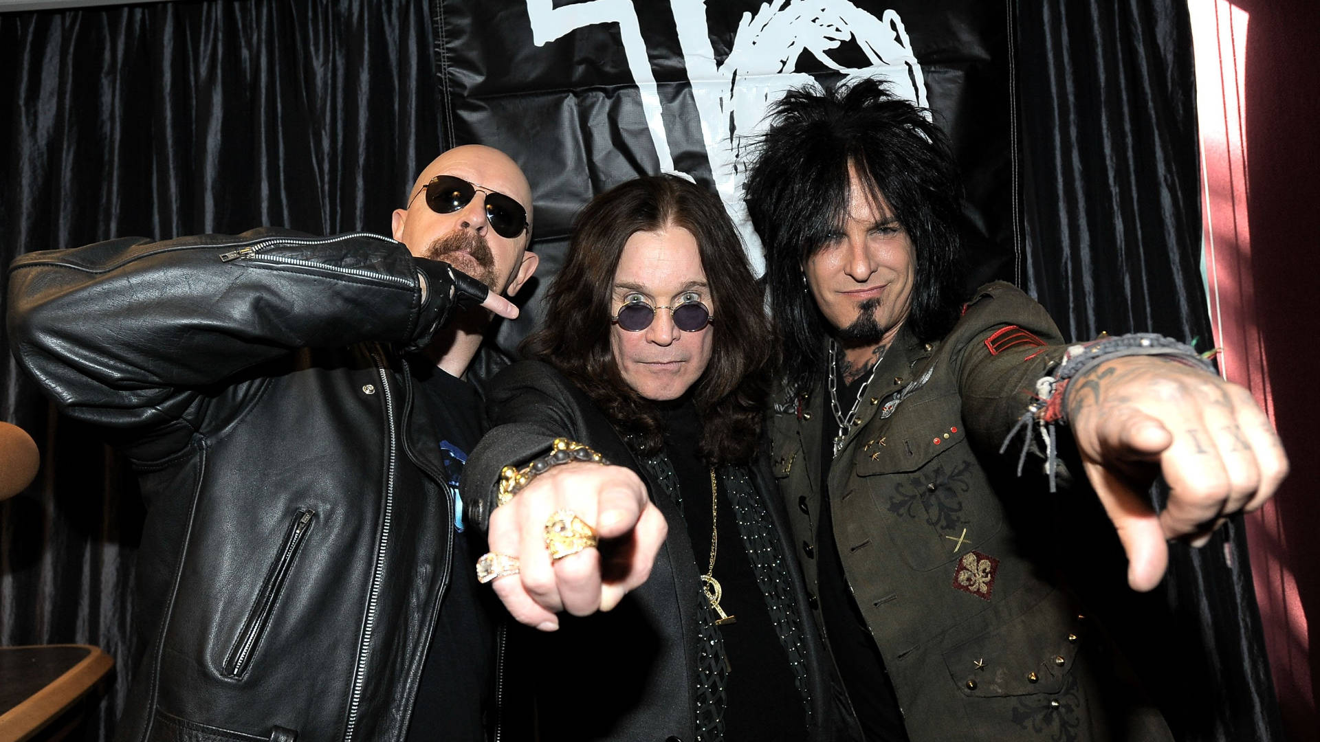 Ozzy Osbourne 桌布 壁紙 — 三位標誌性搖滾音樂家穿著皮夾克和太陽眼鏡，在黑色窗簾背景下自信地擺姿勢。