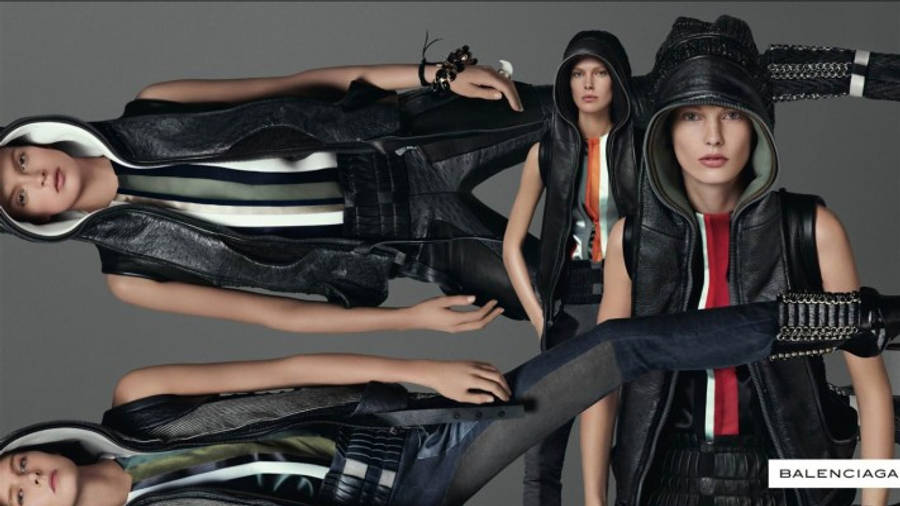 Balenciaga 桌布 壁紙 — 三位模特兒穿著前衛的黑色皮連帽衫和背心，在灰色中性背景前動感擺姿勢。
