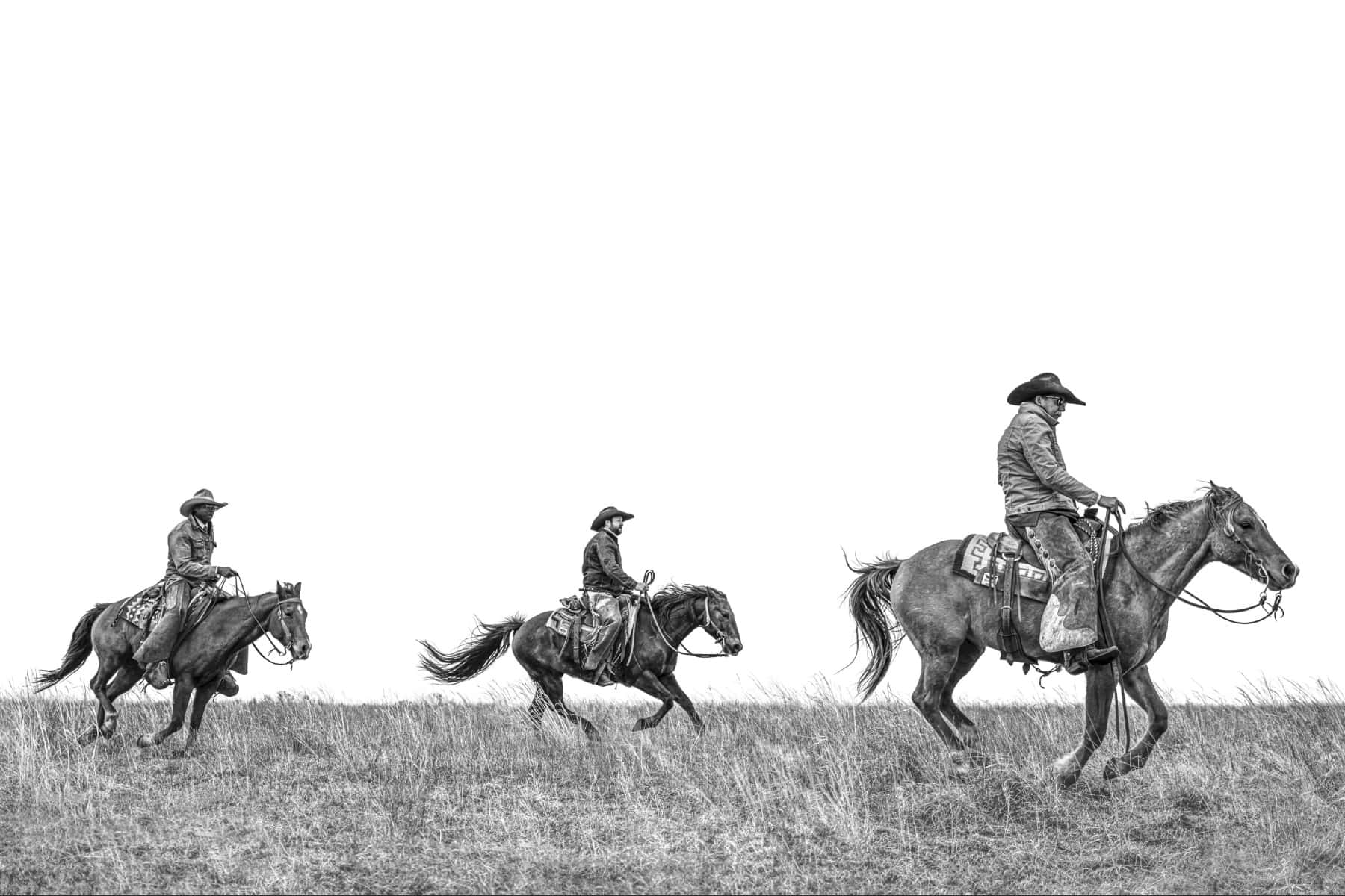 Cowboy 桌布 壁紙 — 三位牛仔騎著馬穿過一片草地，在 stark 白色天空下，以戲劇性的黑白構圖呈現。