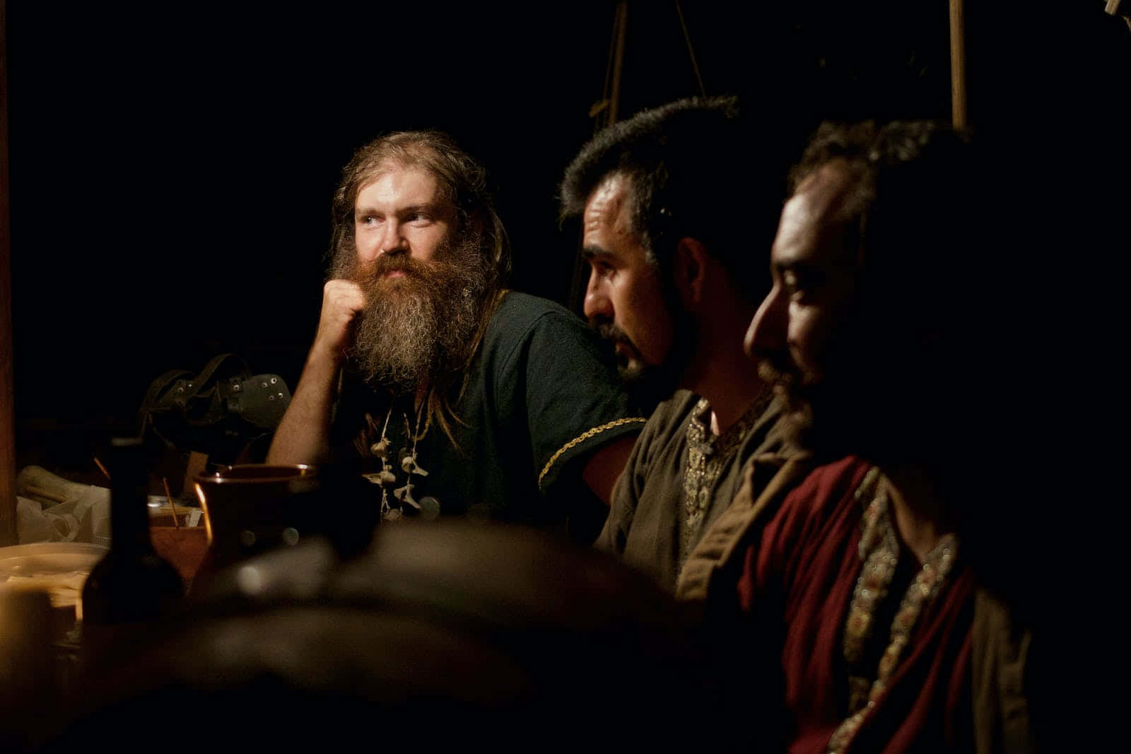 Middle Ages 桌布 壁紙 — 三位留鬍鬚的男人在昏暗燈光下坐在桌旁，其中一人托腮，專注於寧靜的時刻。