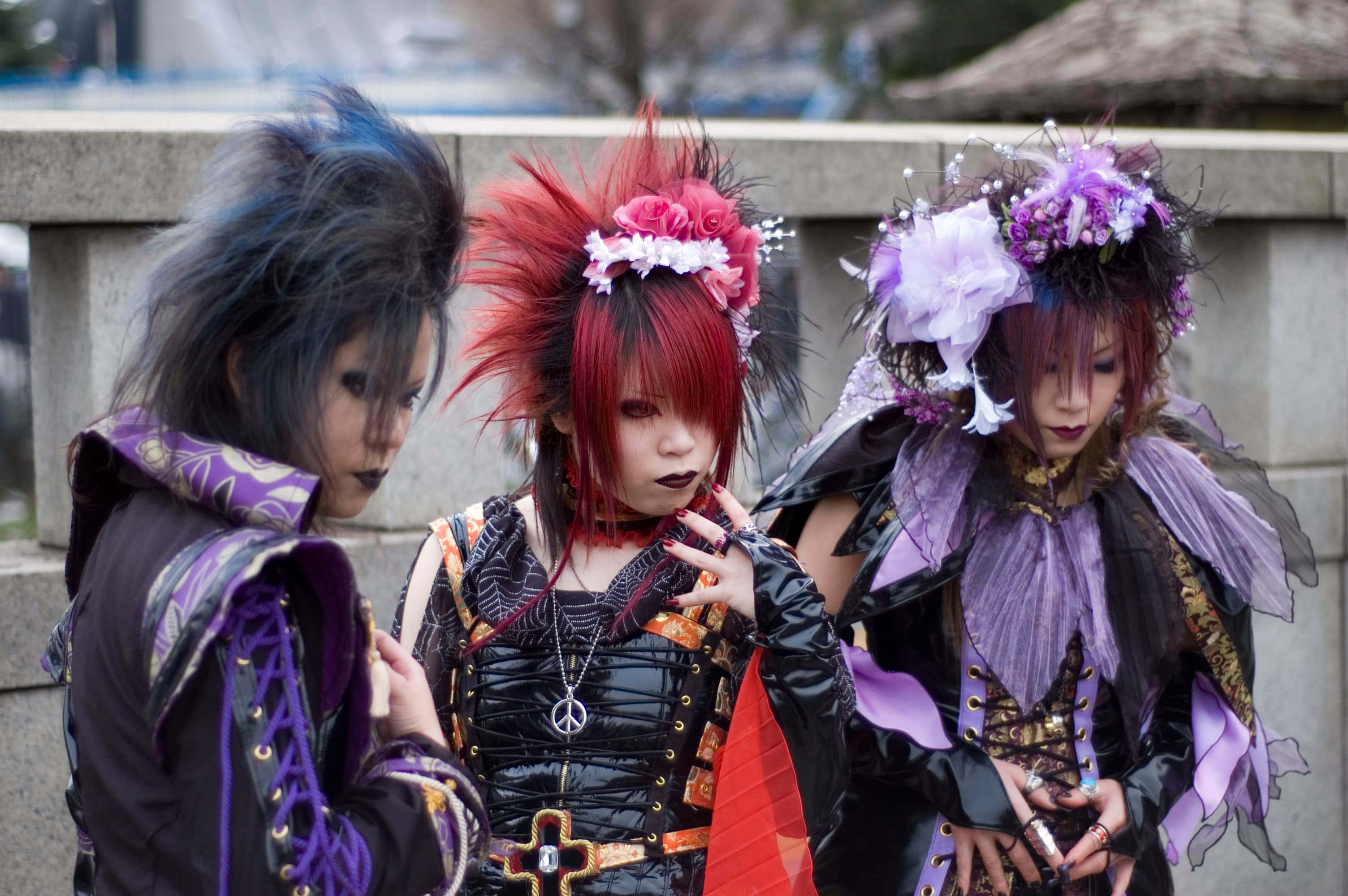 Visual Kei 桌布 壁紙 — 三位穿著精緻哥德蘿莉塔時尚、擁有鮮豔髮色和華麗服飾的人一起站在戶外。