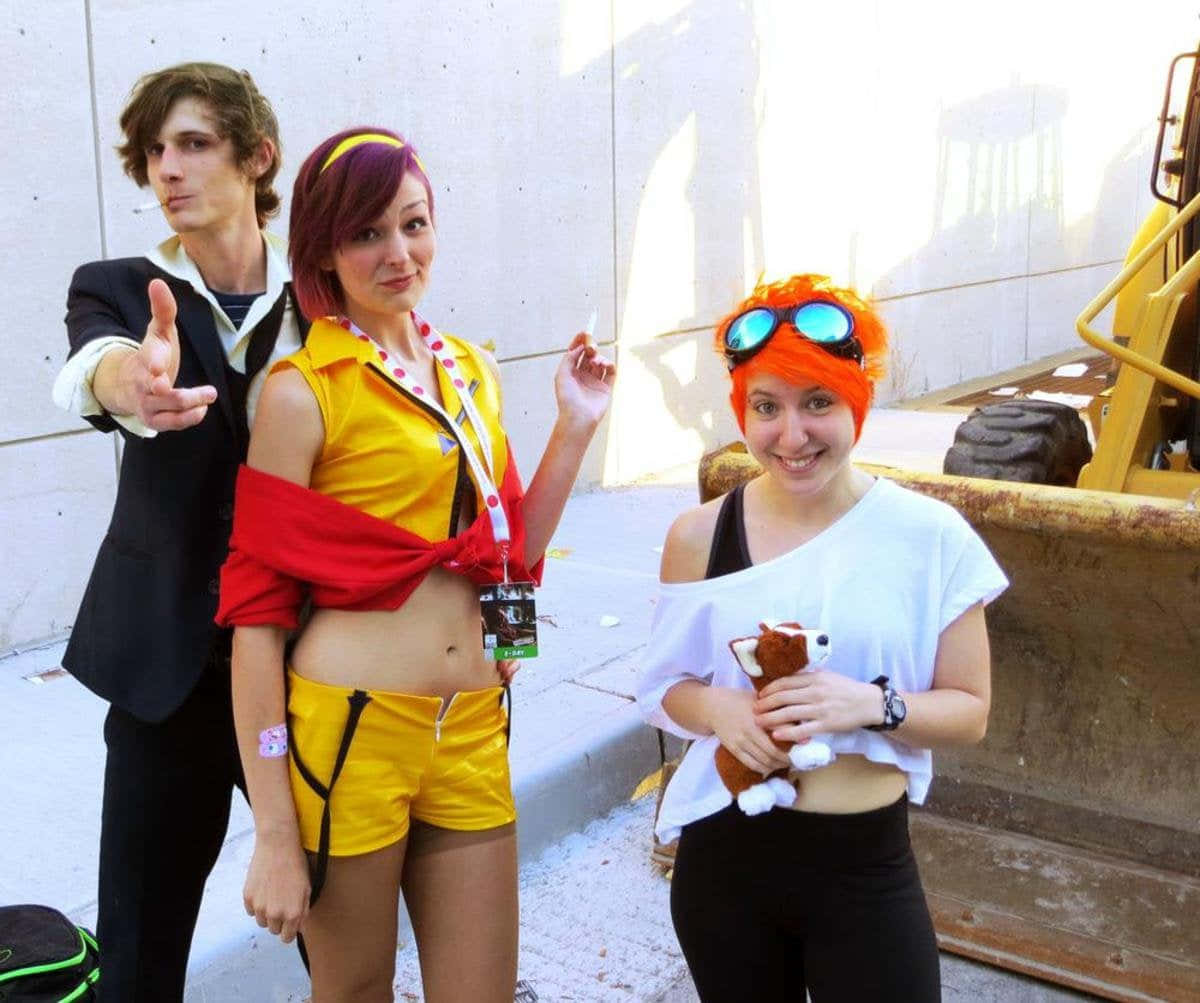 Cowboy Bebop Edward 桌布 壁紙 — 三位穿著鮮豔服裝的cosplayer在明亮的日光下，開心地在一輛黃色工程車旁擺姿勢。