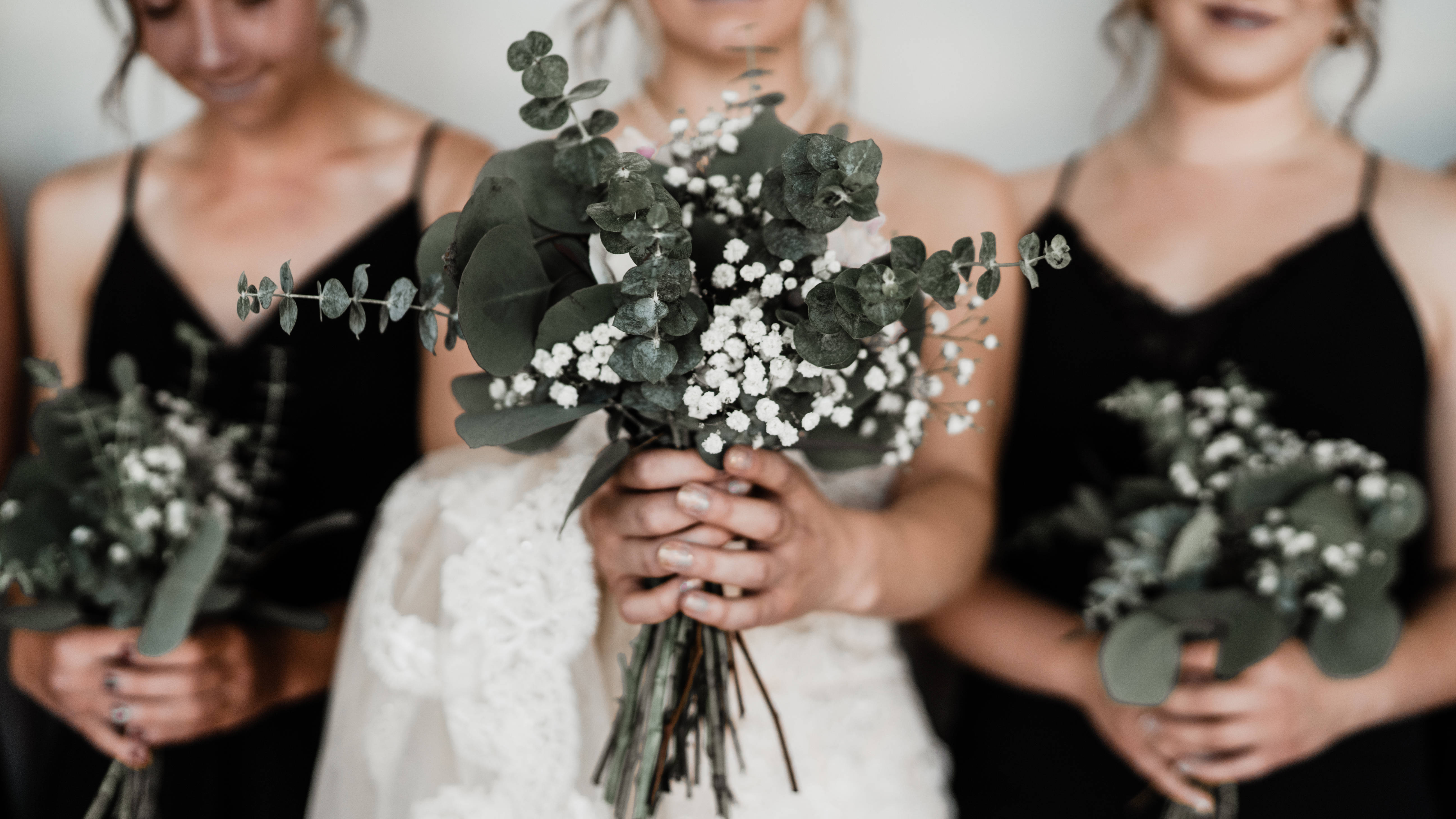 Bridesmaids 桌布 壁紙 — 三位穿著黑色連衣裙的伴娘手持綠色尤加利葉和白色滿天星花束，焦點柔和地落在她們微笑的臉龐上。