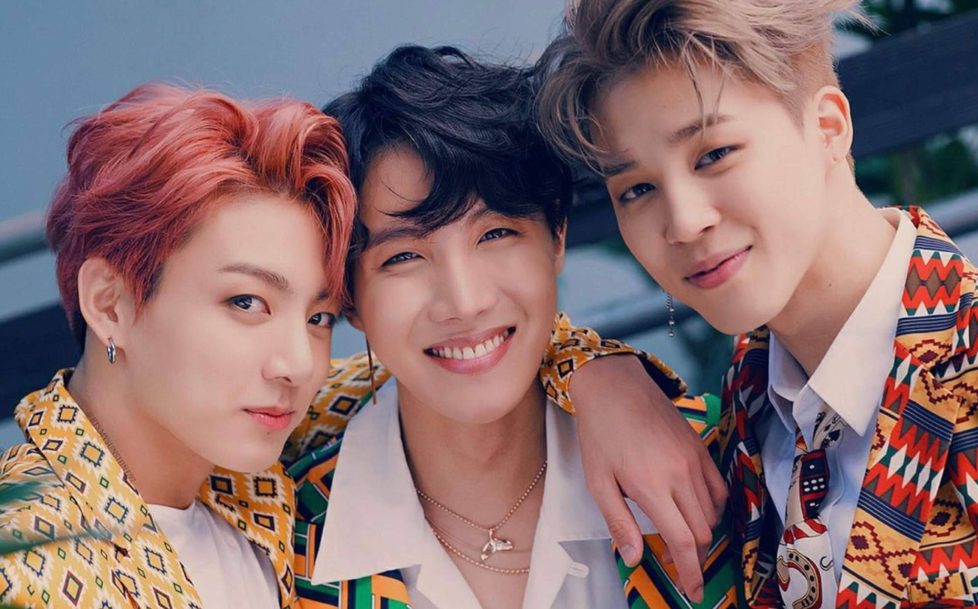 jhope 桌布 壁紙 — 三位笑容滿面、髮色鮮豔、身穿圖案外套的年輕男子在戶外緊密地擺姿勢。