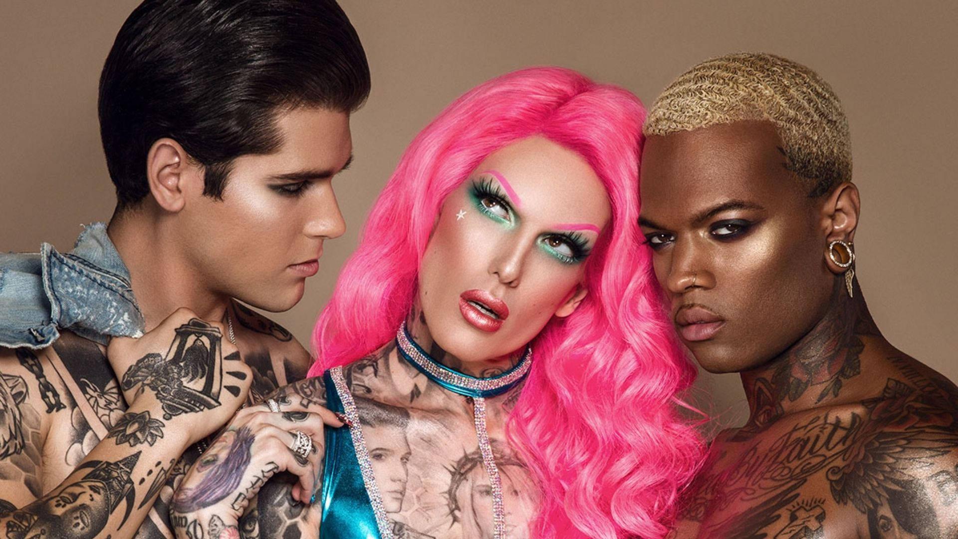 Jeffree Star 桌布 壁紙 — 三位紋身人士緊密擺姿勢，其中一人有亮粉紅色頭髮和閃亮化妝，被兩位眼神銳利的男士夾在中間，背景為中性色調。