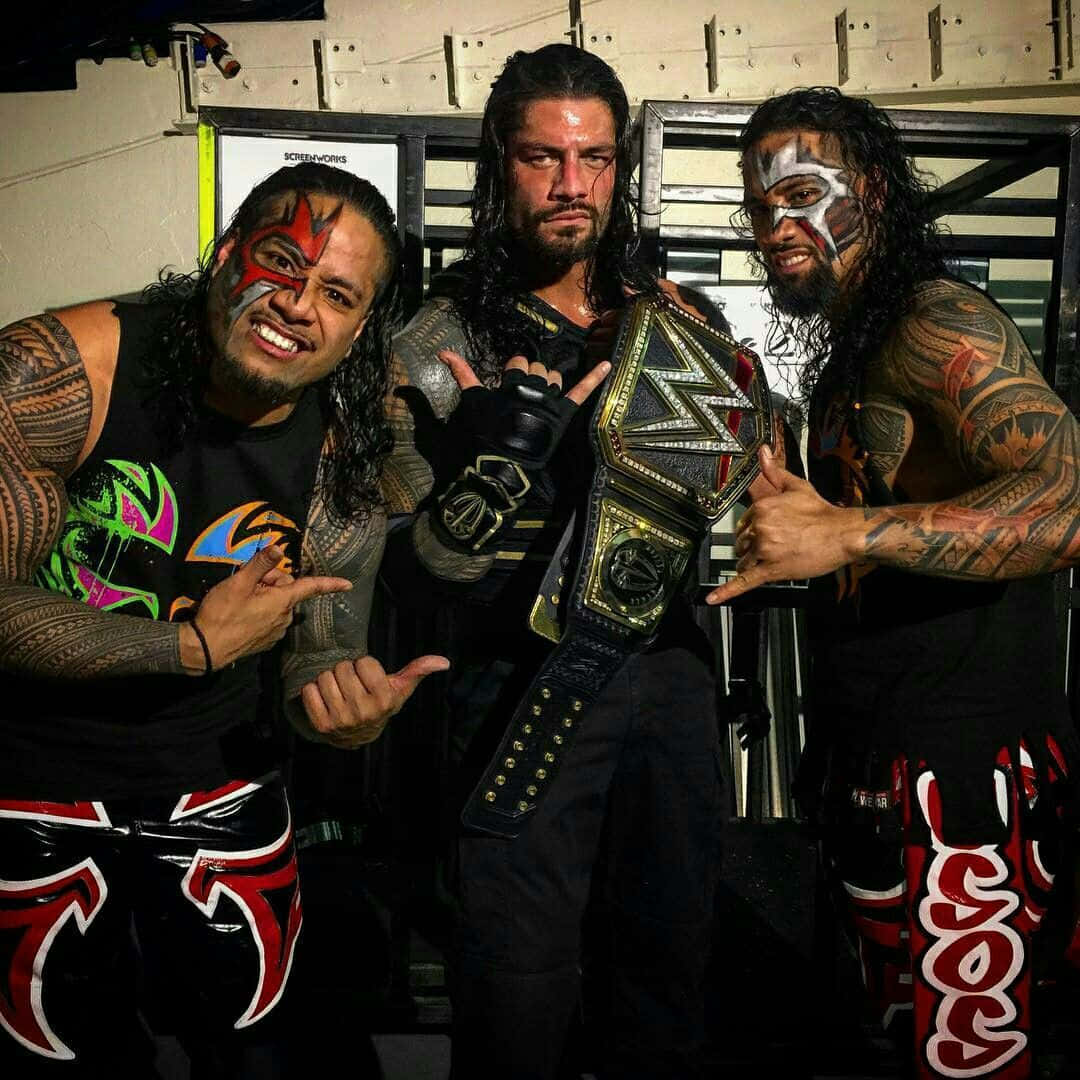 WWE 桌布 壁紙 — 三位紋身摔角手帶著臉部彩繪，在後台區域自信地擺姿勢，手持冠軍腰帶。