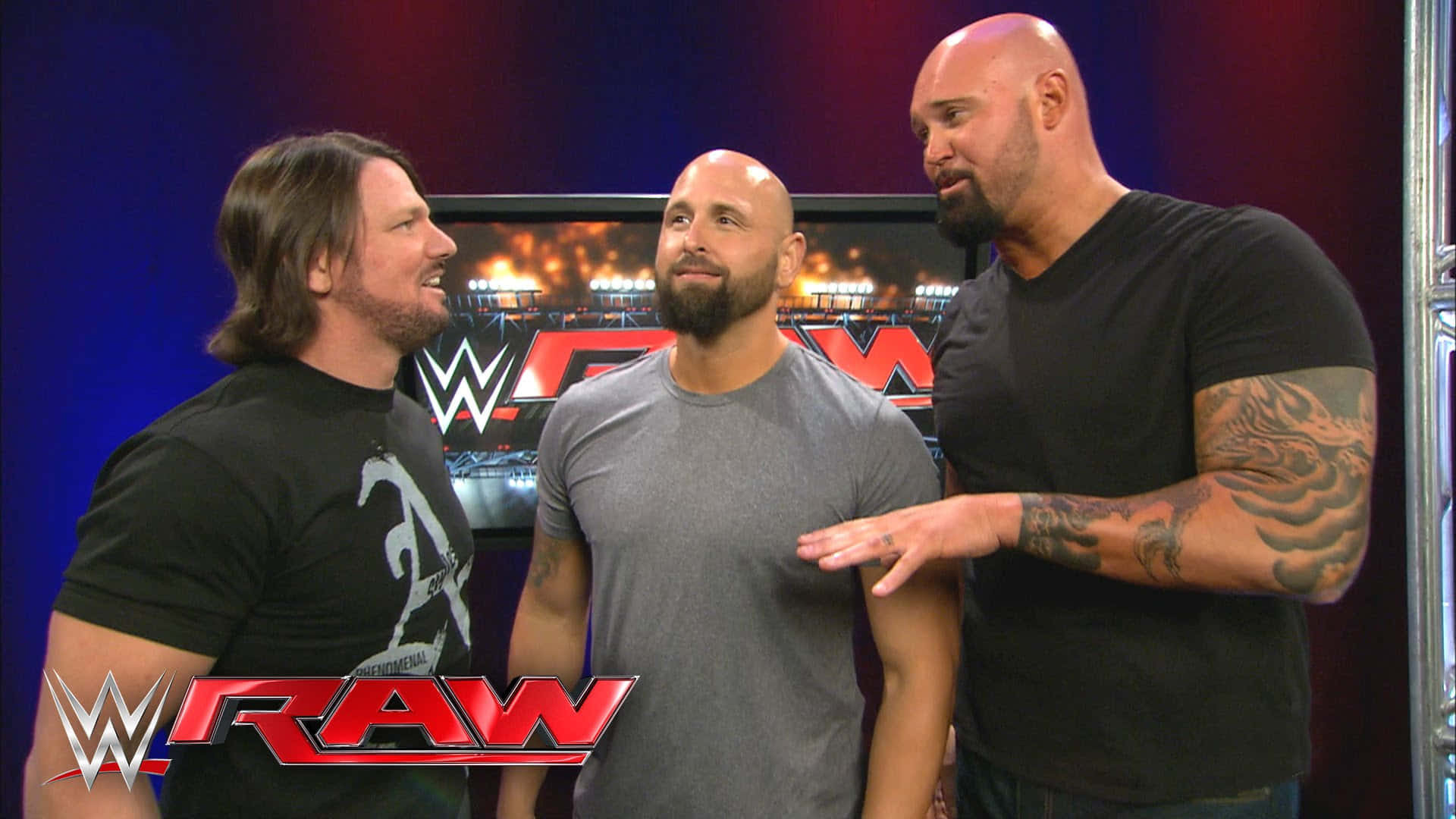 WWE 桌布 壁紙 — 三位肌肉發達的WWE摔角手身穿黑色和灰色T恤，站在帶有'RAW'品牌標誌和火焰背景圖形的攝影棚場景中。