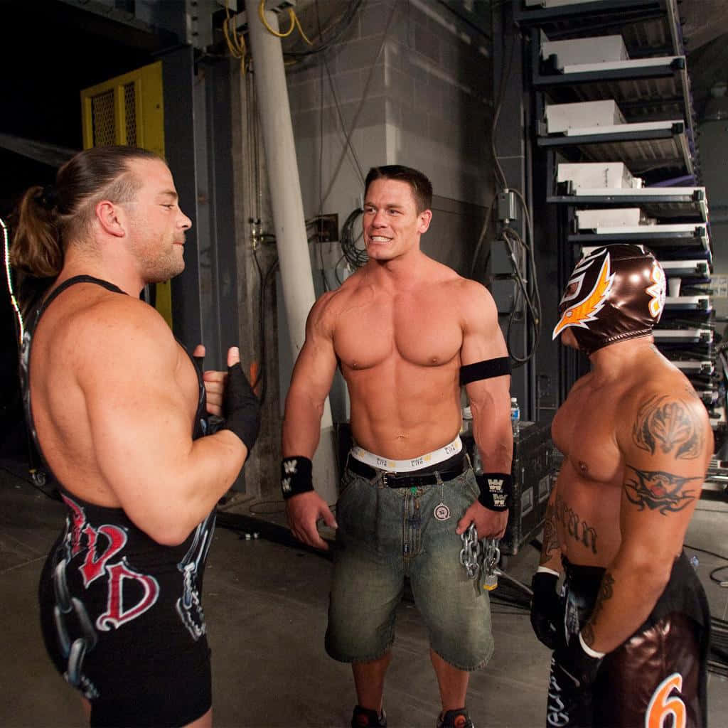 WWE 桌布 壁紙 — 三位肌肉發達的摔角手在後台區域，帶有刺青和裝備，在緊張的時刻互相對峙。