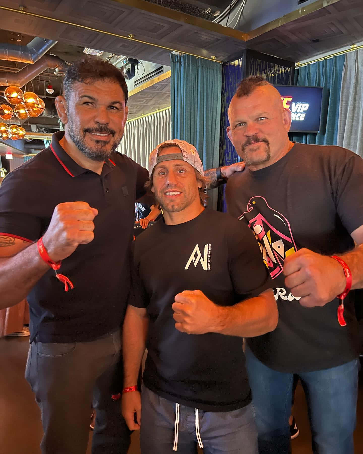 MMA 桌布 壁紙 — 三位肌肉發達的男士在一個現代化的室內場地，在吊燈和藍色窗簾背景下自信地舉起拳頭擺姿勢。