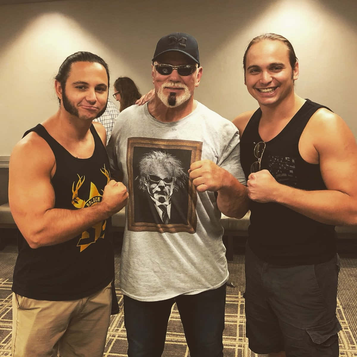 WWE 桌布 壁紙 — 三位肌肉發達的男士在室內擺姿勢，其中一人手持一個戴太陽眼鏡的男士的裱框肖像。