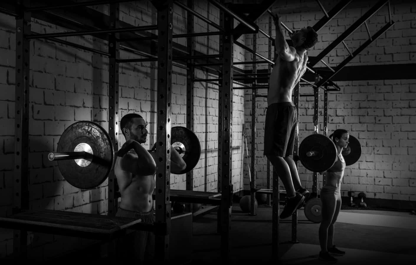 Fitness 桌布 壁紙 — 三位肌肉發達的運動員在一個粗糙的黑白健身房中進行高強度訓練，健身房有裸露的磚牆和沉重的槓鈴。