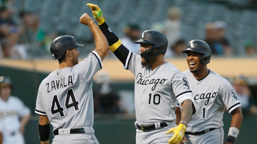 Chicago White Sox 桌布 壁紙 — 三位芝加哥白襪棒球球員在陽光明媚的球場上以擊掌和笑容慶祝一次攻勢。
