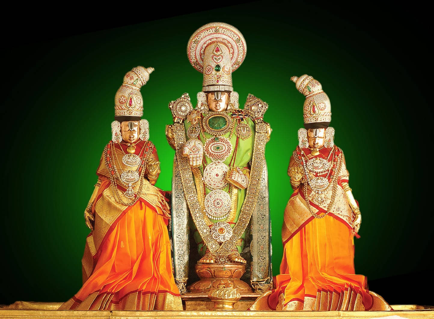 Venkateswara 桌布 壁紙 — 三位華麗的金色印度教神祇，身著鮮豔的橙色和綠色服飾，莊嚴地站在深綠色背景前。