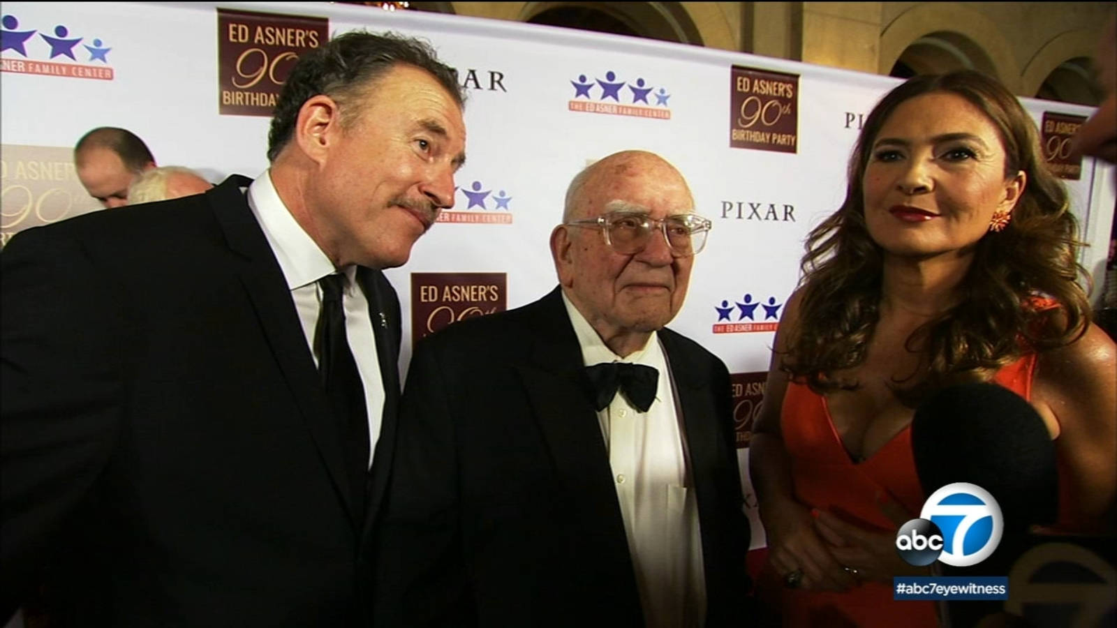 abc 桌布 壁紙 — 三位衣著正式的名人在 Ed Asner 的 90 歲生日派對上，在一個有品牌標誌的紅地毯上合照。