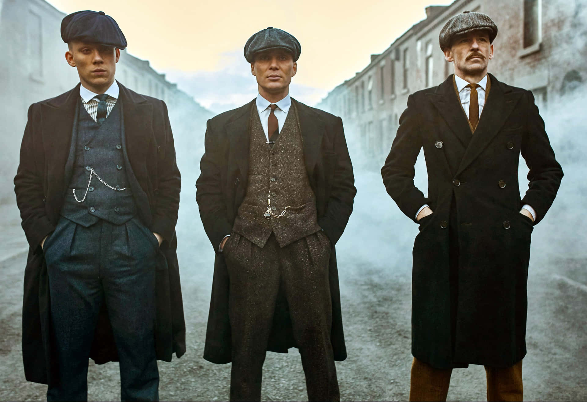 三位身穿復古西裝和扁平帽的男子站在霧氣瀰漫的街道上。 — Peaky Blinders 壁紙