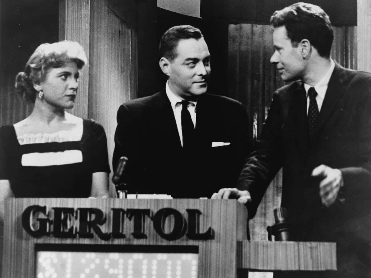 1950s 桌布 壁紙 — 三位身穿復古西裝的人站在帶有「GERITOL」品牌的講台上，參加經典電視遊戲節目。