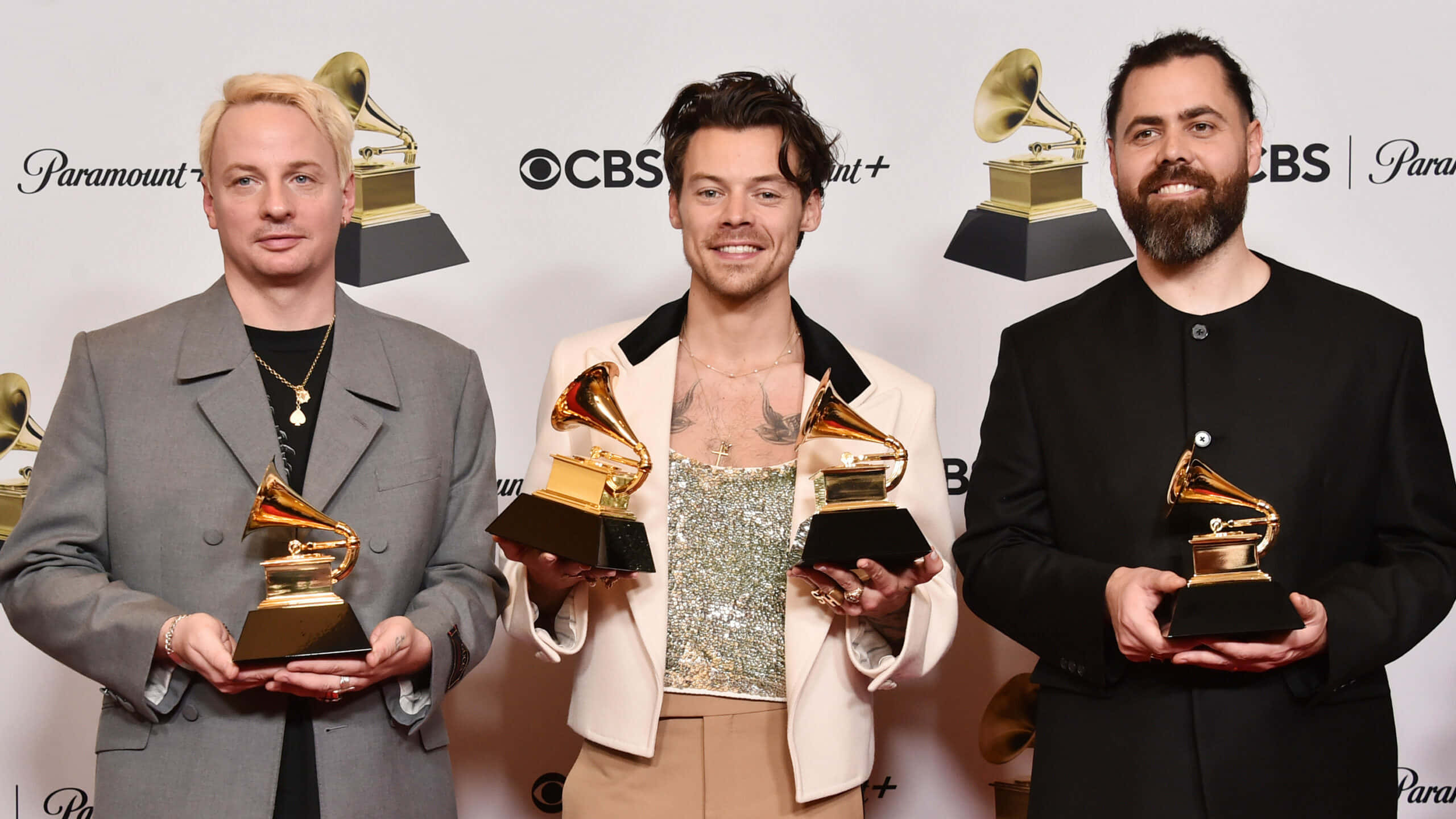Harry Styles 2021 桌布 壁紙 — 三位身穿時尚服裝的男士在品牌活動背景前與葛萊美獎盃合影。