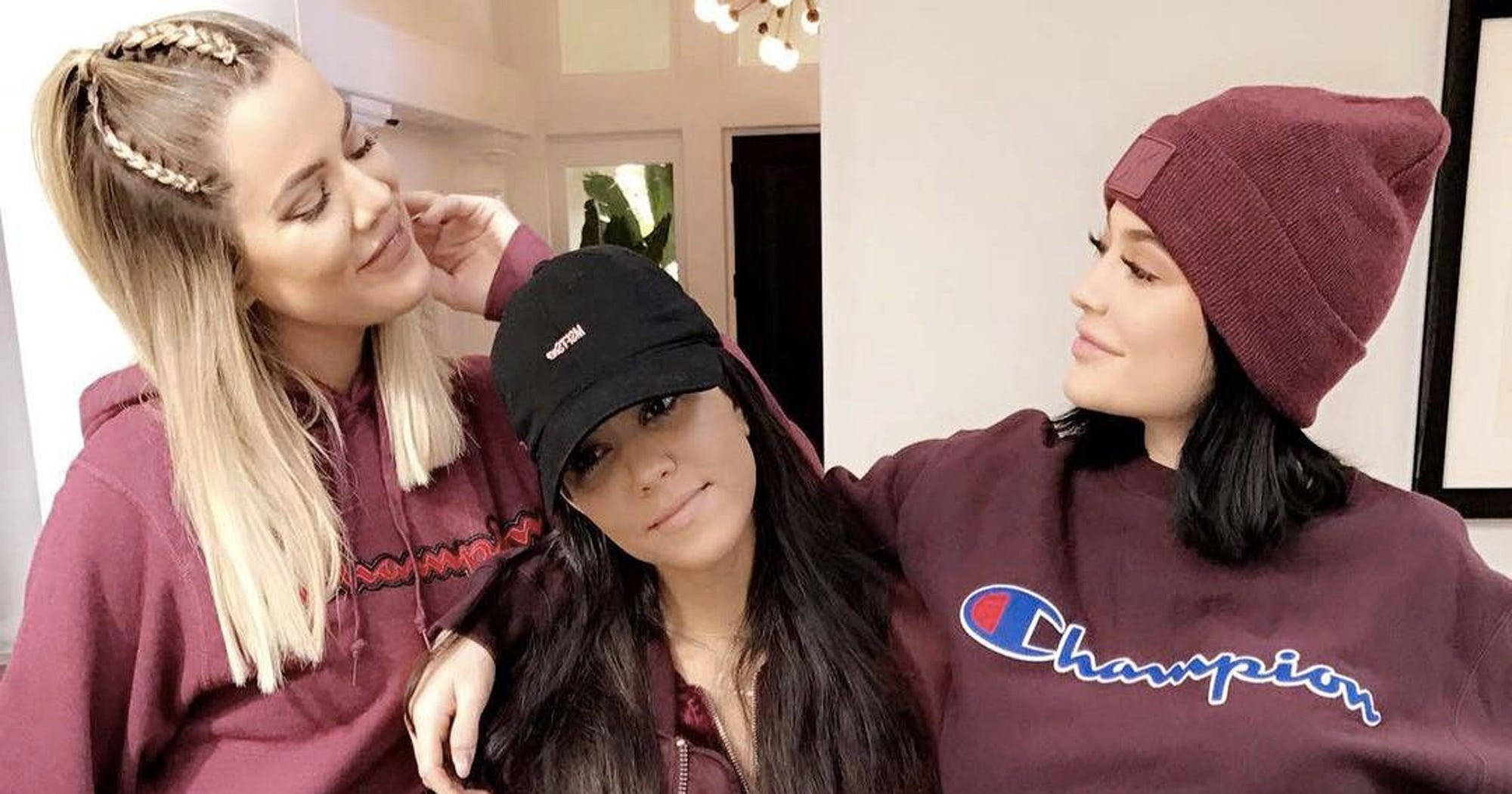 Champion Logo 桌布 壁紙 — 三位身穿栗色連帽上衣和毛帽的女性在室內柔和燈光下分享溫馨親密的時刻。