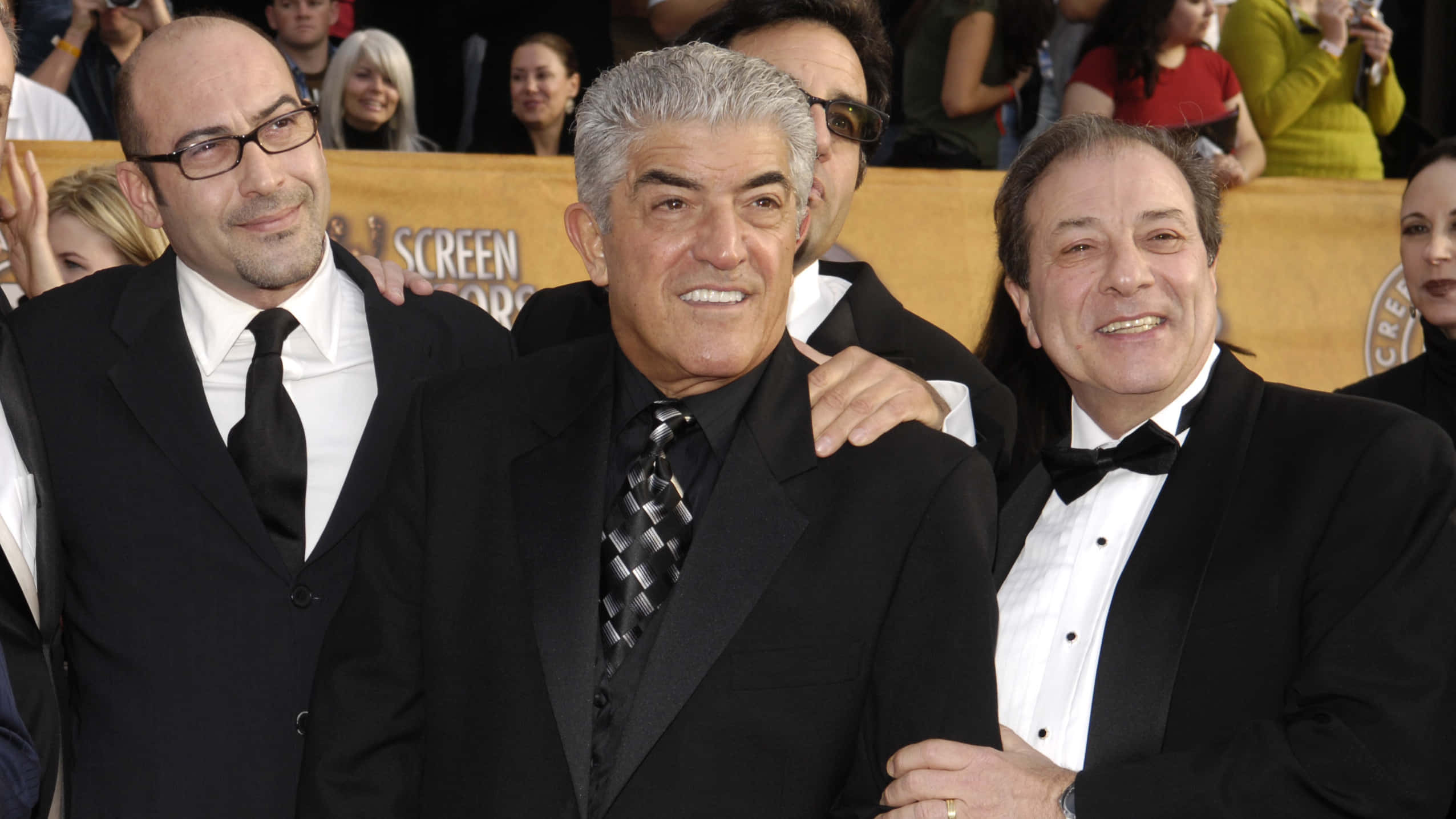 Frank Vincent 桌布 壁紙 — 三位身穿正式黑色禮服的笑容滿面男士在金色背景的紅地毯活動中一起擺姿勢。