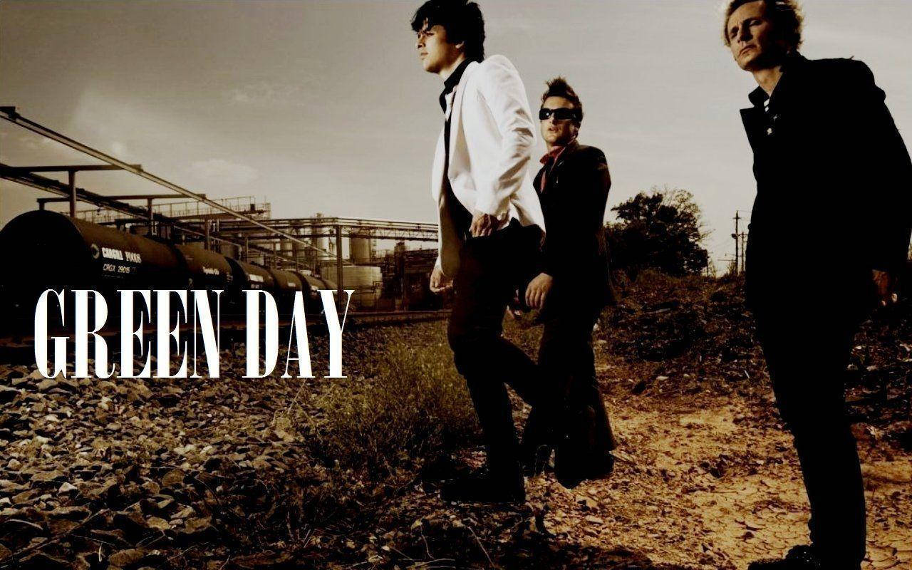 Green Day 桌布 壁紙 — 三位身穿深色西裝的樂團成員自信地站在礫石上，旁邊是生鏽的火車車廂，天空朦朧。