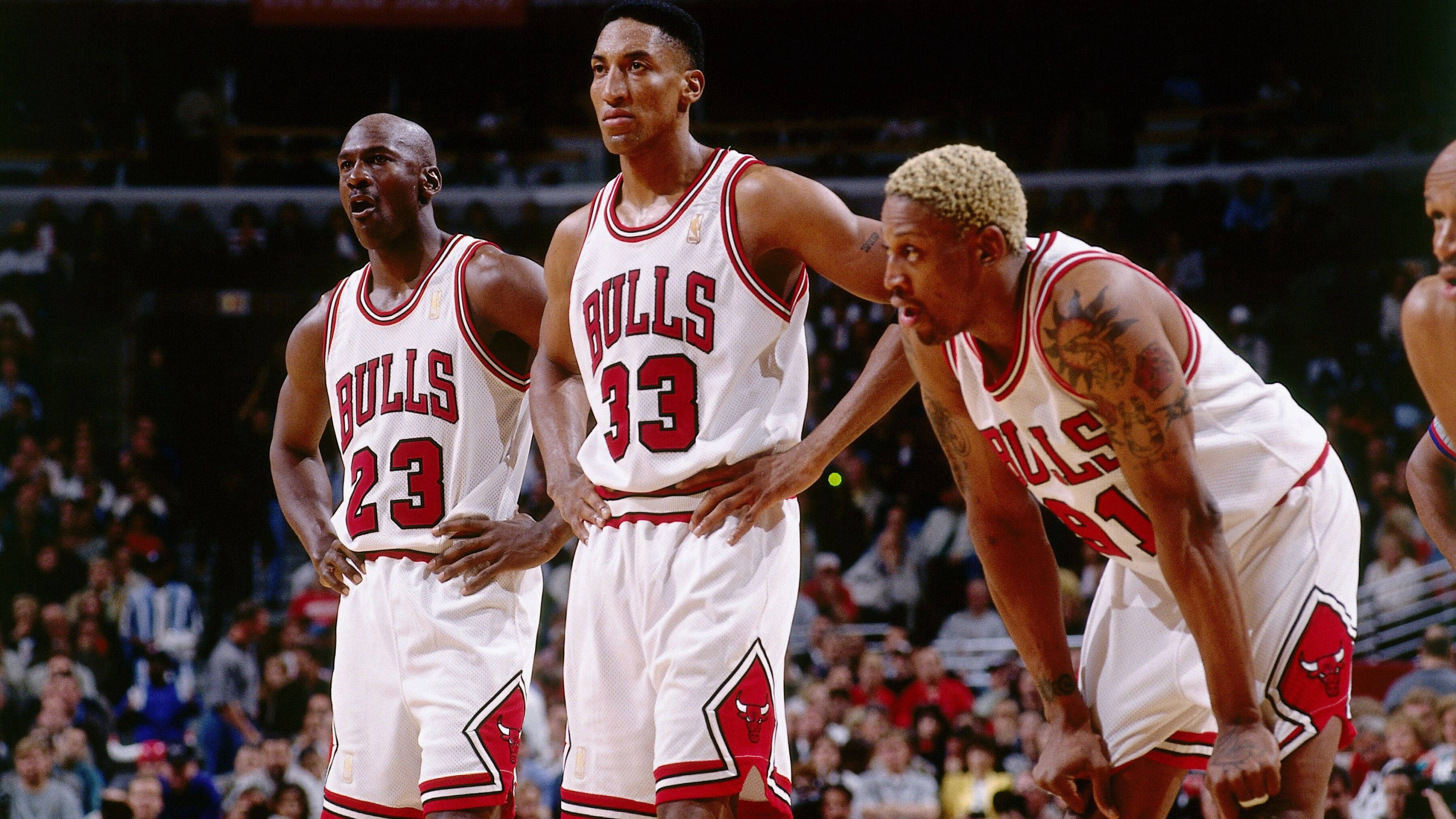 NBA 桌布 壁紙 — 三位身穿白色和紅色球衣的芝加哥公牛籃球運動員在比賽中專注地比賽，背景有觀眾。