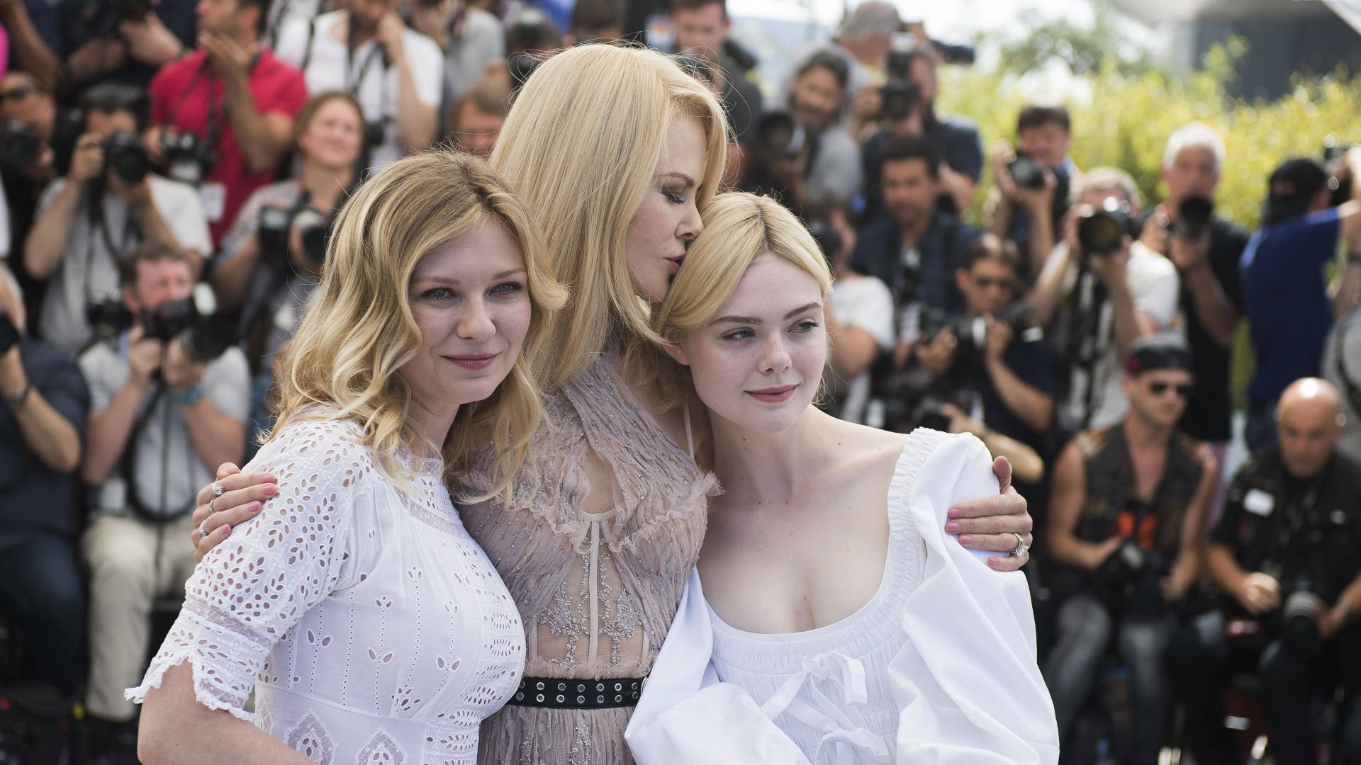 Kirsten Dunst 桌布 壁紙 — 三位身穿白色連衣裙的女性在攝影師包圍的紅地毯上緊密地擺姿勢。