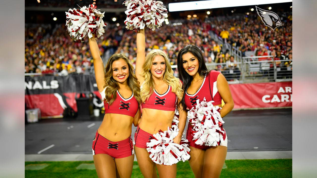 Cheerleader 桌布 壁紙 — 三位身穿紅色制服、面帶微笑的啦啦隊員在足球場上拿著彩球，身後是座無虛席的體育場。