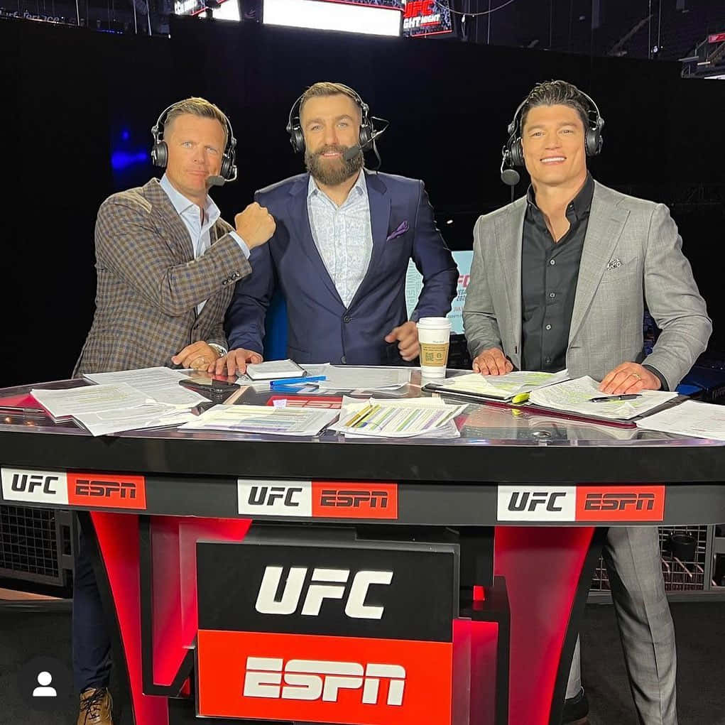 UFC 桌布 壁紙 — 三位身穿西裝、戴著耳機的男性評論員坐在UFC ESPN播報桌前，桌上放有文件和咖啡杯。