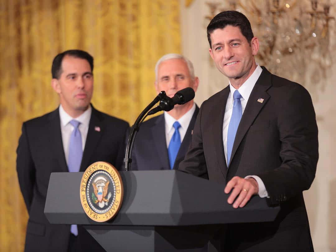 桌布 壁紙 — 三位身穿西裝的男子站在總統講台前，身後有金色窗簾和吊燈。