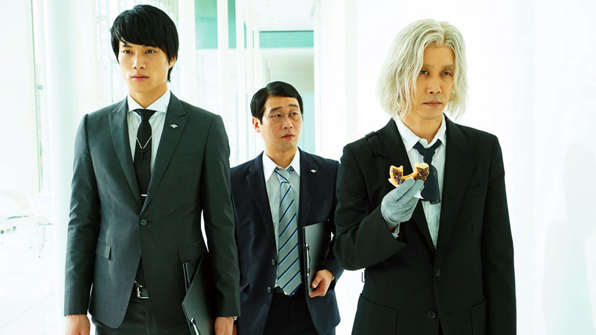 Tokyo Ghoul Movie 桌布 壁紙 — 三位身穿西裝的男子走過明亮的現代辦公室，其中一人正在吃零食，另外兩人向前看。